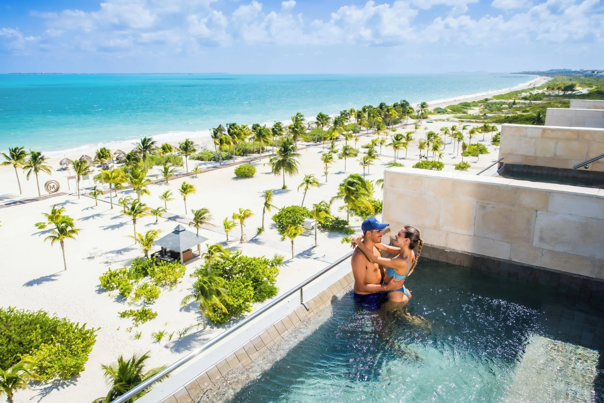 Oceanfront plunge pool at Majestic Elegance Costa Mujeres with couple and panoramic beach view.