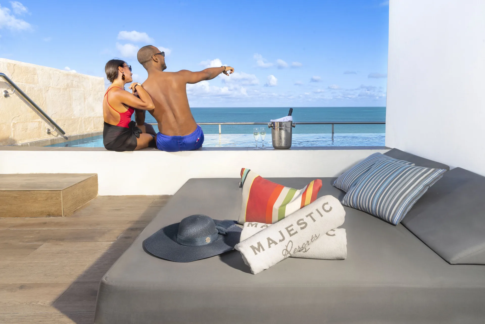 Terrace daybed and oceanfront plunge pool at Majestic Elegance Costa Mujeres with guests by the water.