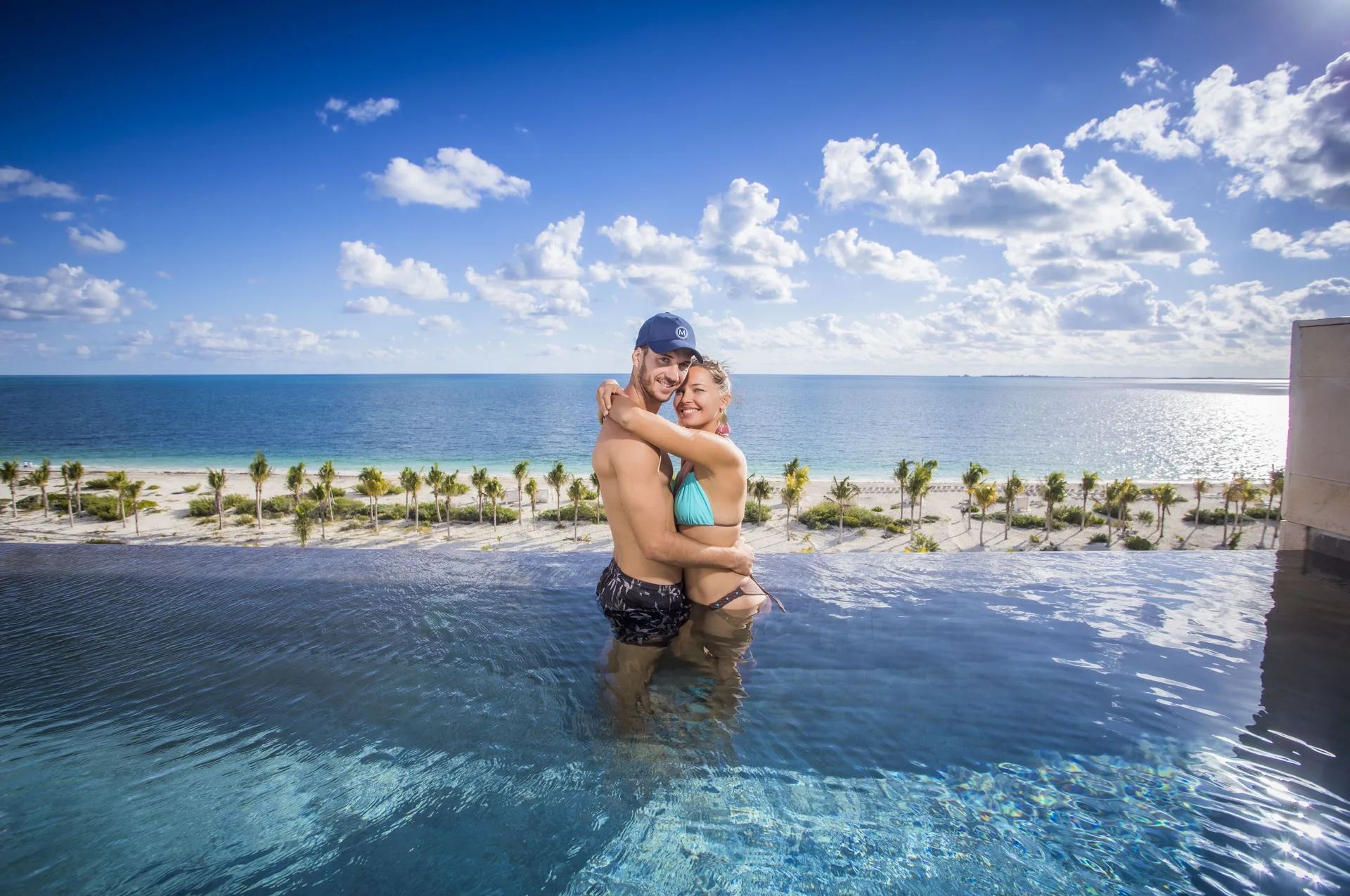 Couple in an oceanfront plunge pool at Majestic Elegance Costa Mujeres overlooking the beach.