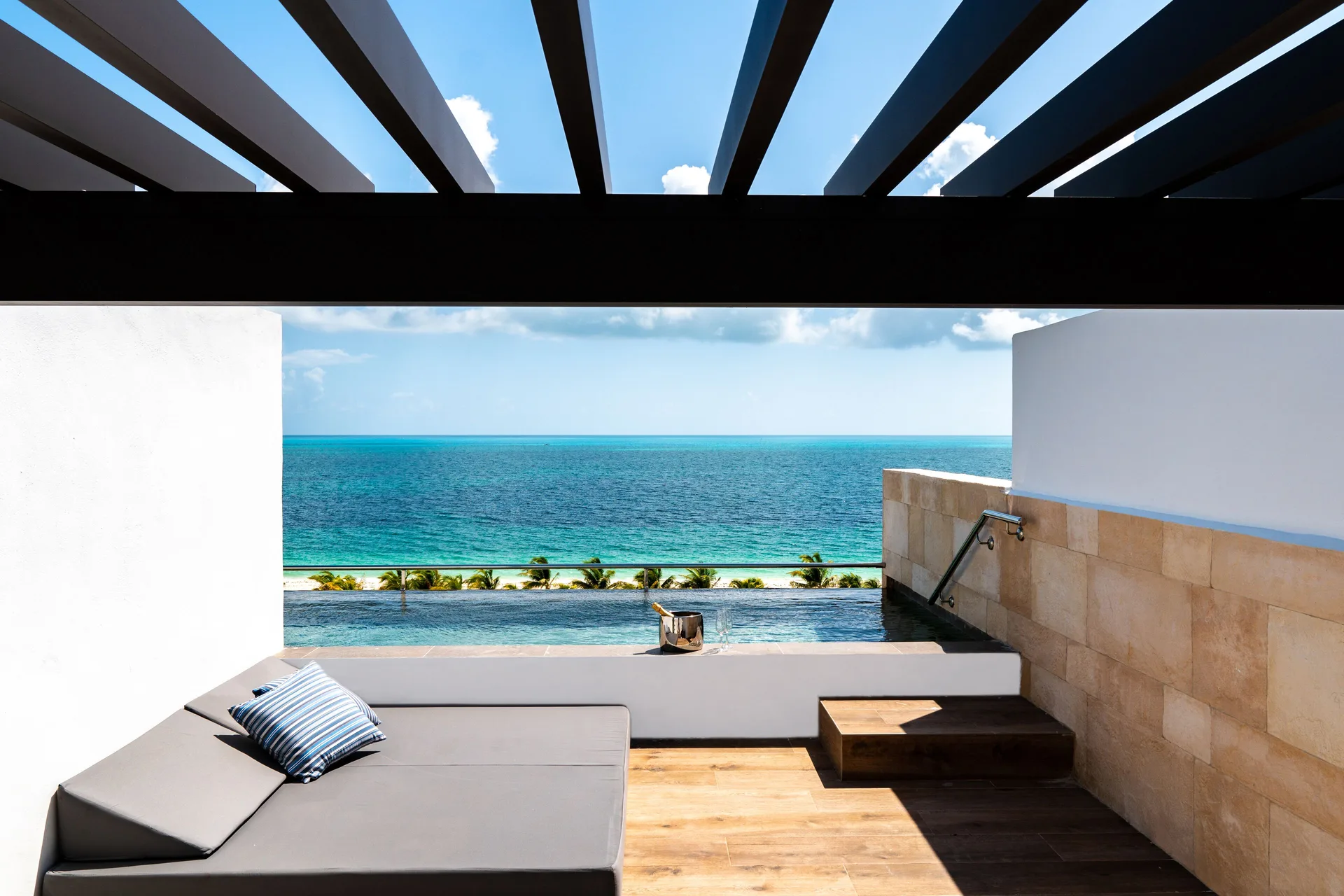 Oceanfront plunge pool terrace at Majestic Elegance Costa Mujeres with daybed and sea view.