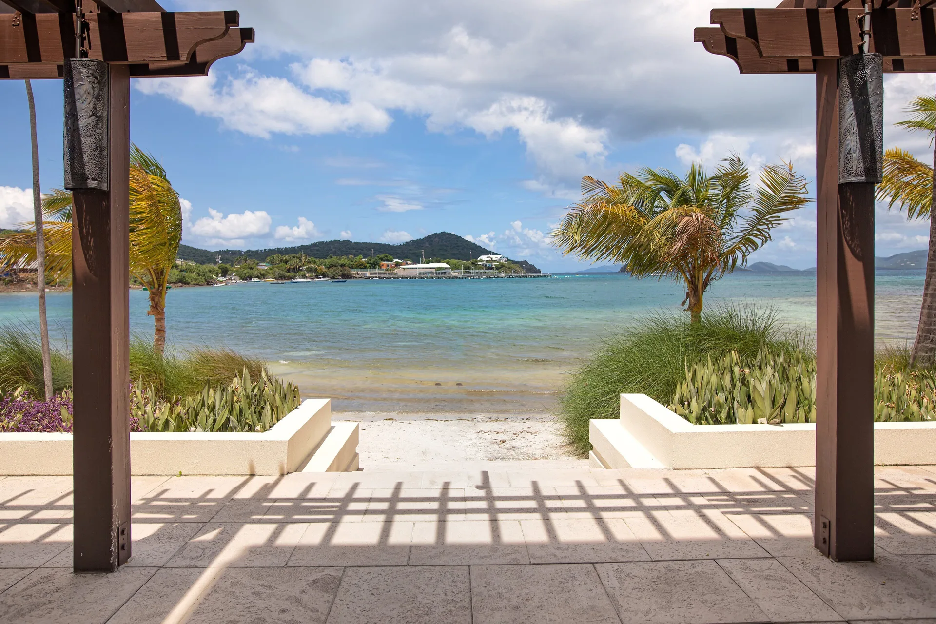 A pergola frames steps to a small beach and turquoise water at Margaritaville Vacation Club - St. Thomas.