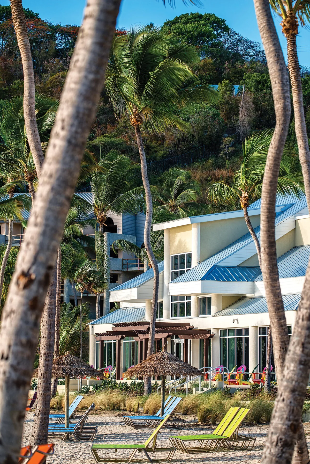 Beach loungers, thatched umbrellas, palms, and resort building at Margaritaville Vacation Club - St. Thomas.