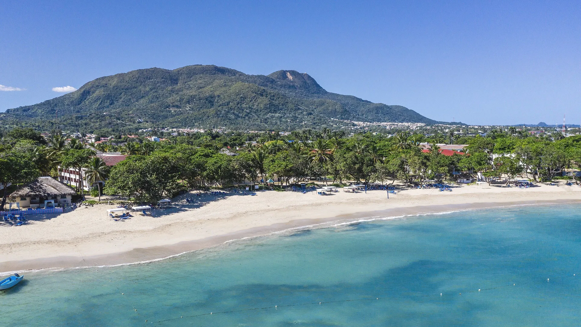 Aerial view of beach, turquoise water, palms, and mountains by Marien Puerto Plata.