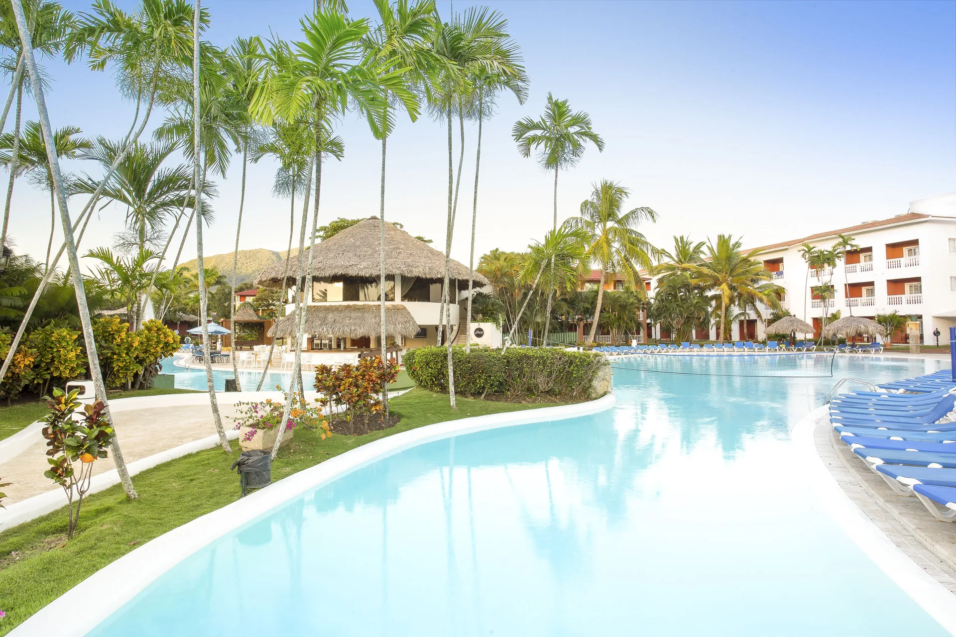 Pool edged by palms, blue loungers, thatched roofs, and guest buildings at Marien Puerto Plata.