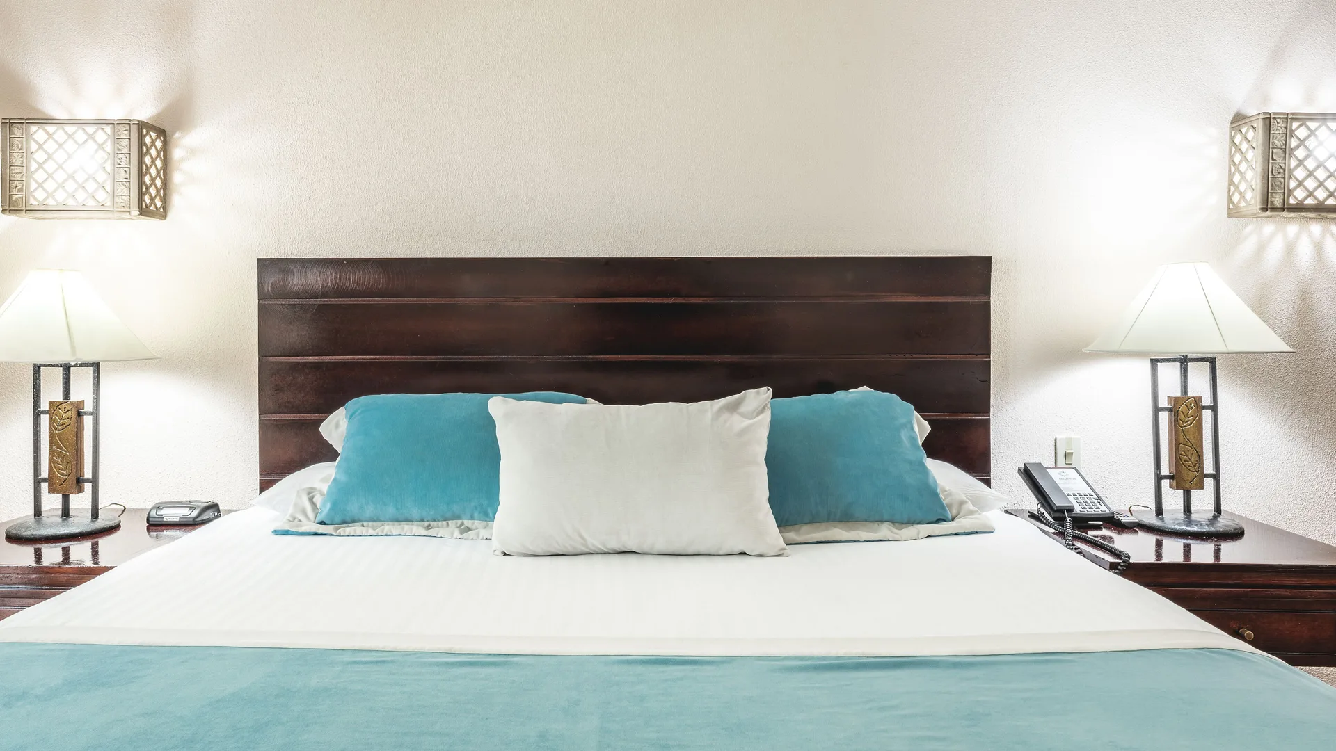 King bed with turquoise pillows and bedside lamps in a Deluxe Ocean View room at Marien Puerto Plata.