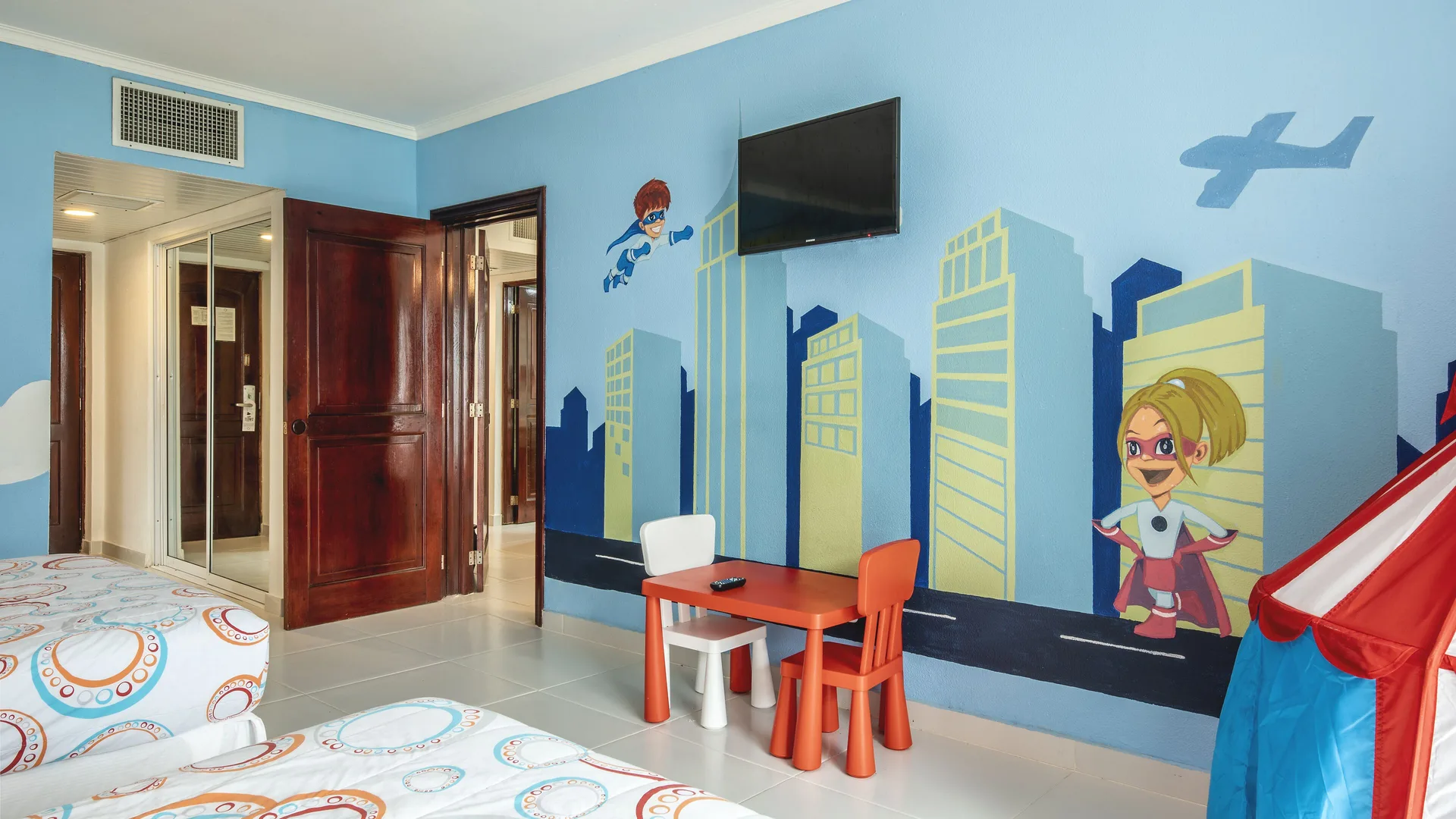 Kids' room with twin beds, superhero mural, small table, and wall-mounted TV at Marien Puerto Plata.