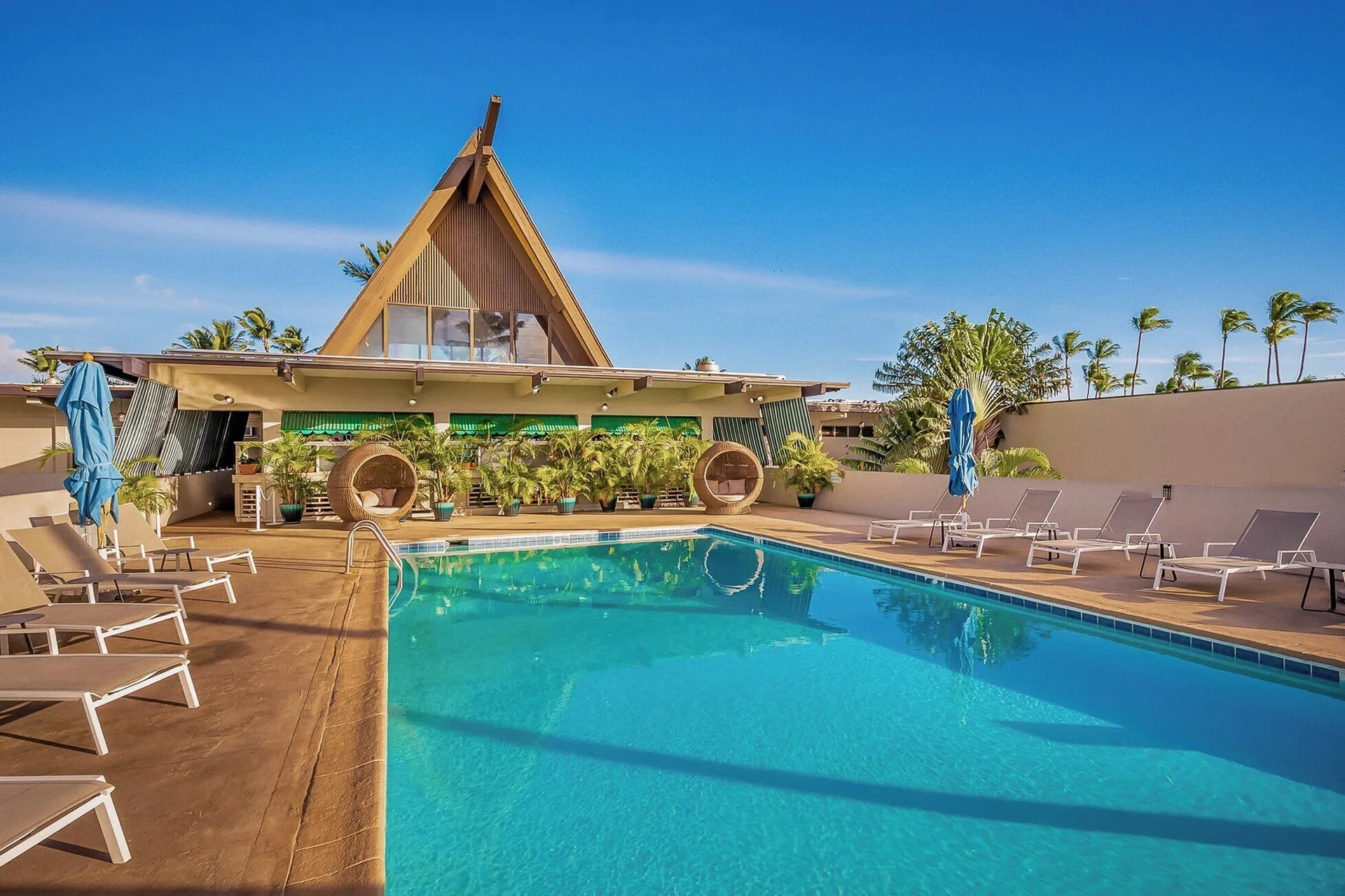 Sunny pool with lounge chairs and peaked-roof building at Maui Beach Hotel.