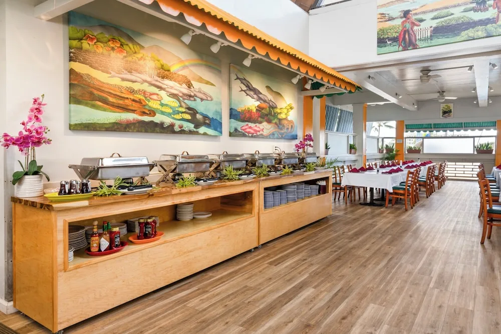 Buffet counter with warmers and Hawaiian murals in a dining room at Maui Beach Hotel.