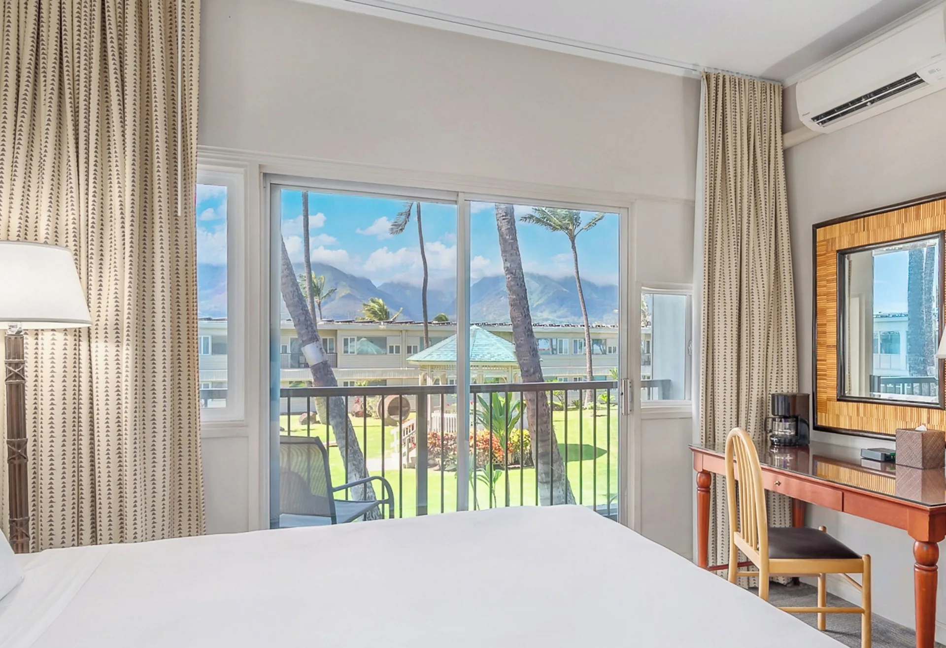 Garden View One room at Maui Beach Hotel with bed, balcony, desk, and lawn view through sliding doors.