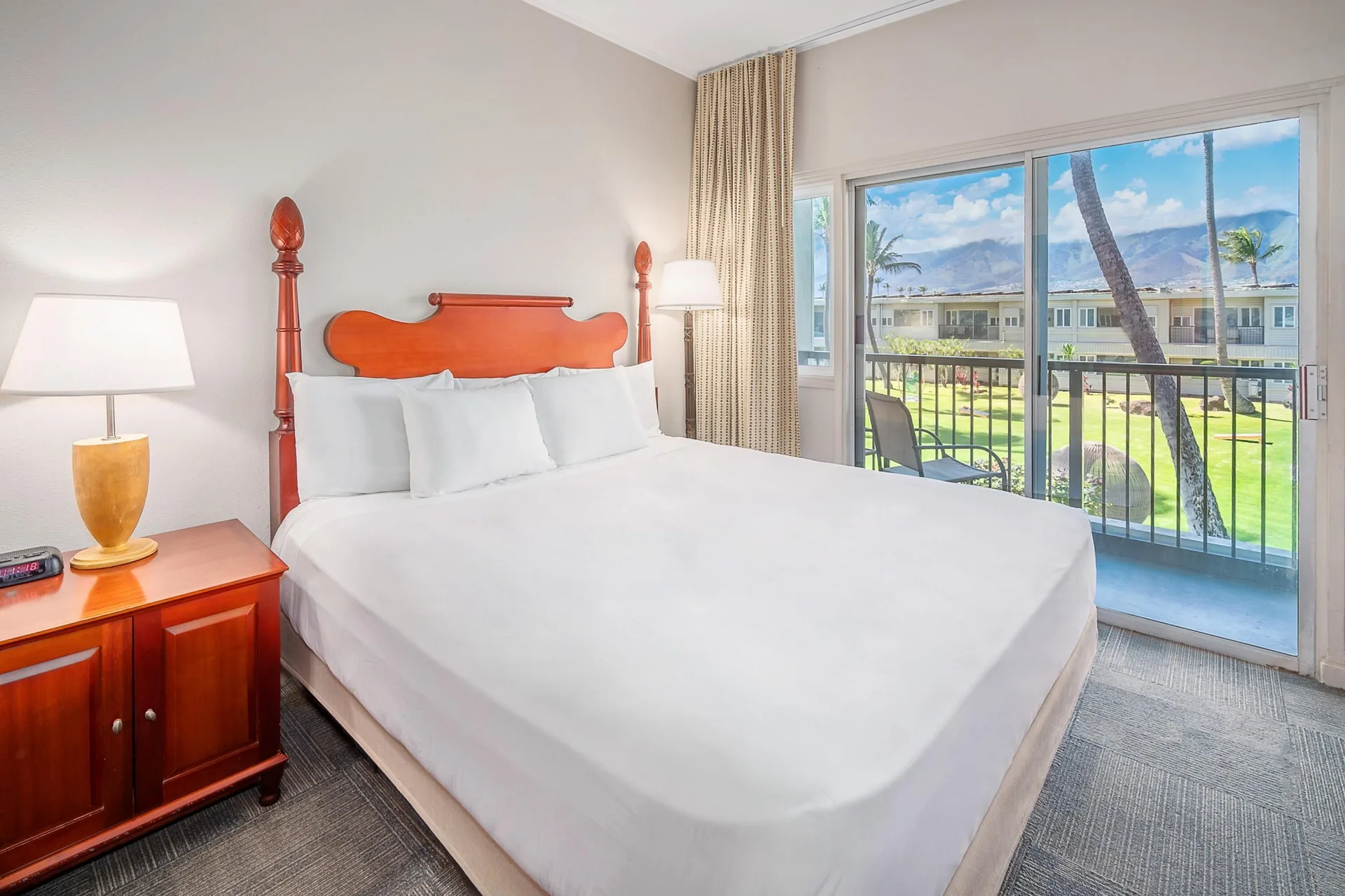 Garden View One room at Maui Beach Hotel with a king bed, nightstand, and balcony facing the lawn.