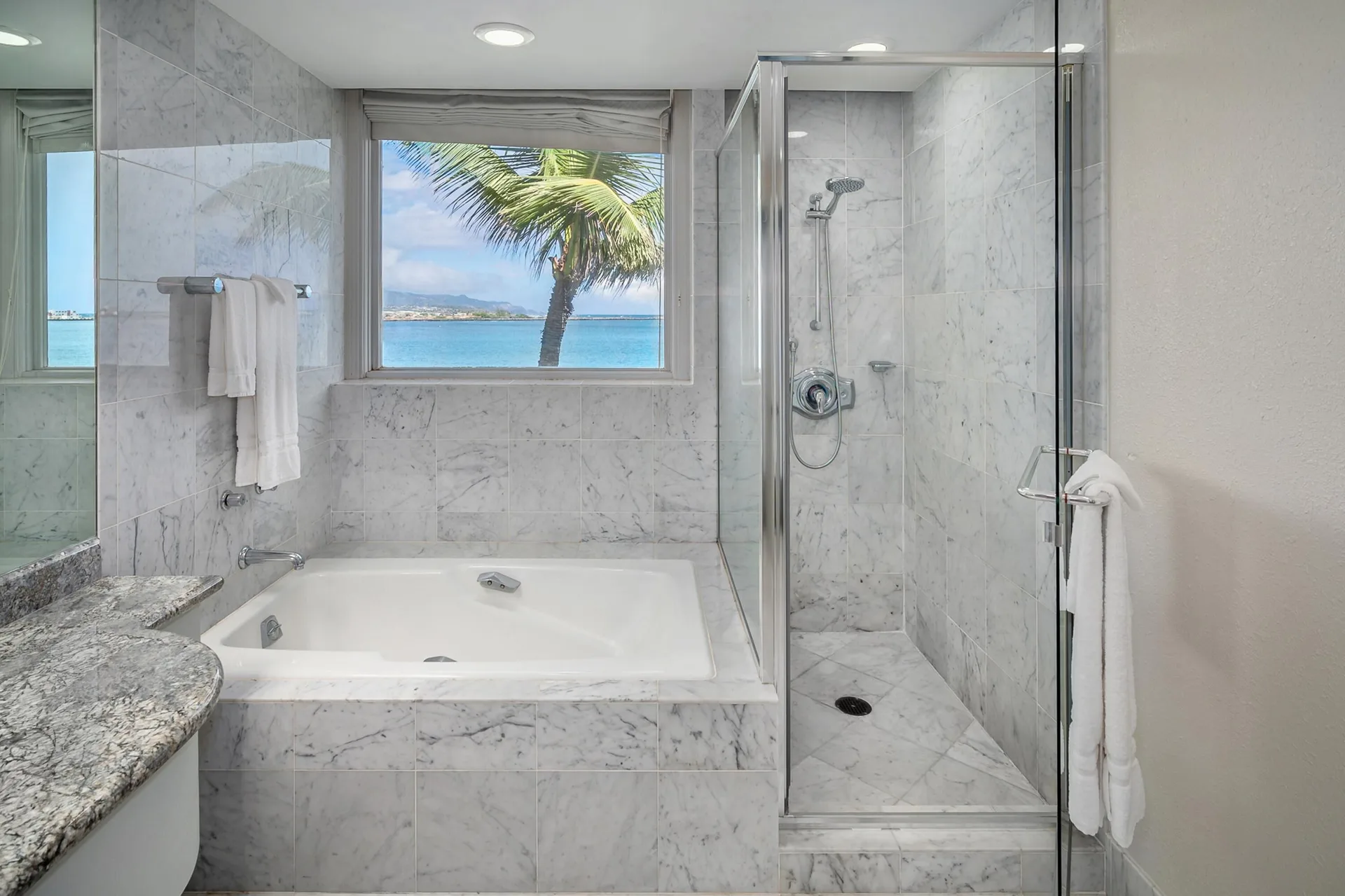 Oceanfront suite bathroom with tub, glass shower, and ocean window at Maui Beach Hotel.