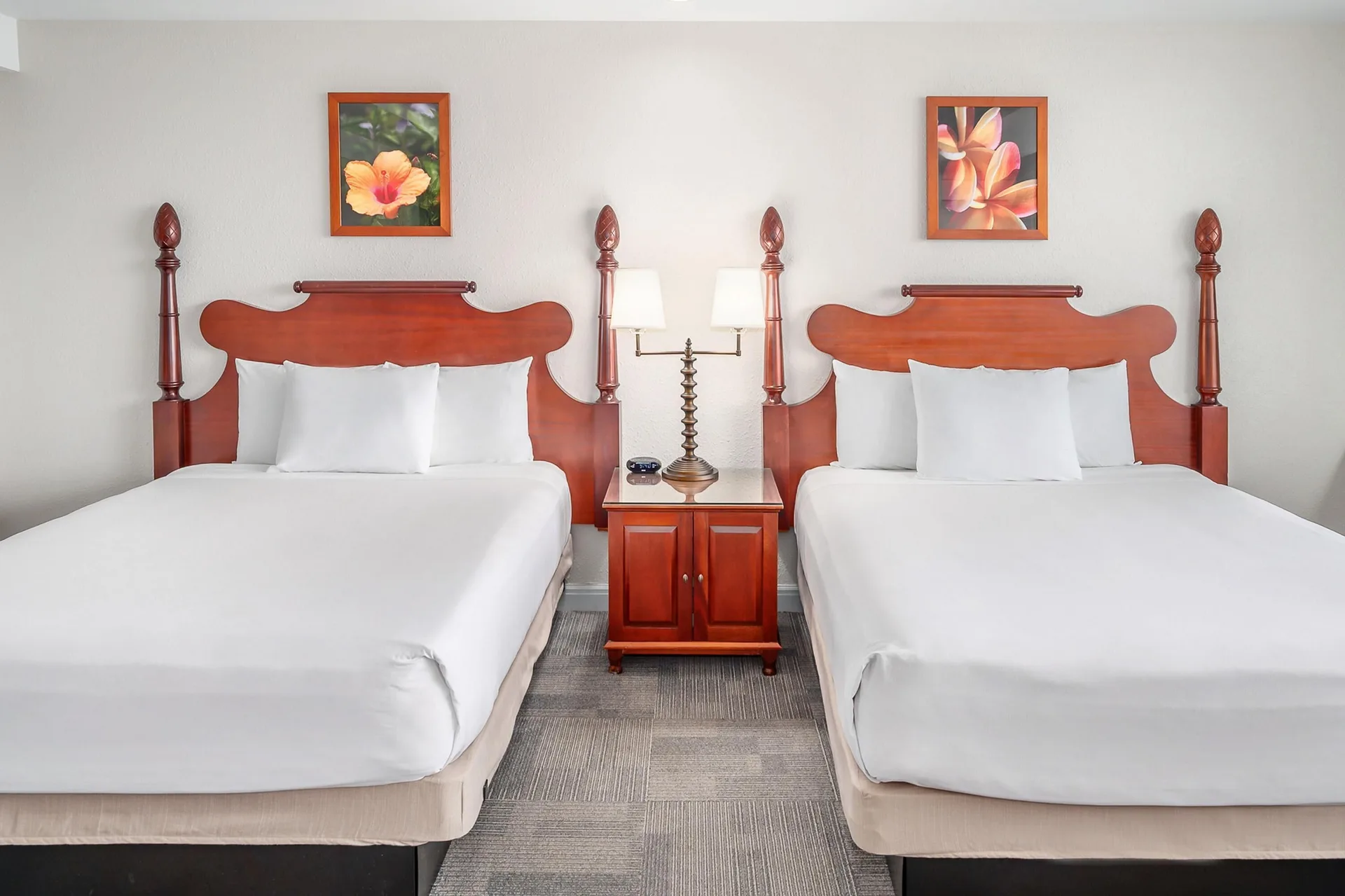 Two white beds with wooden headboards in an oceanfront suite at Maui Beach Hotel.