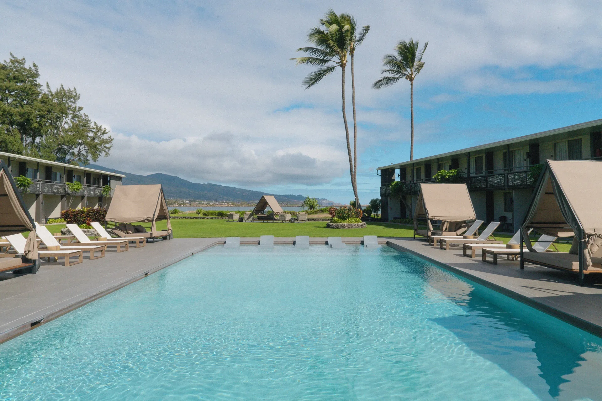 Swimming pool with cabanas, loungers, palms, and water beyond at Maui Seaside Hotel.