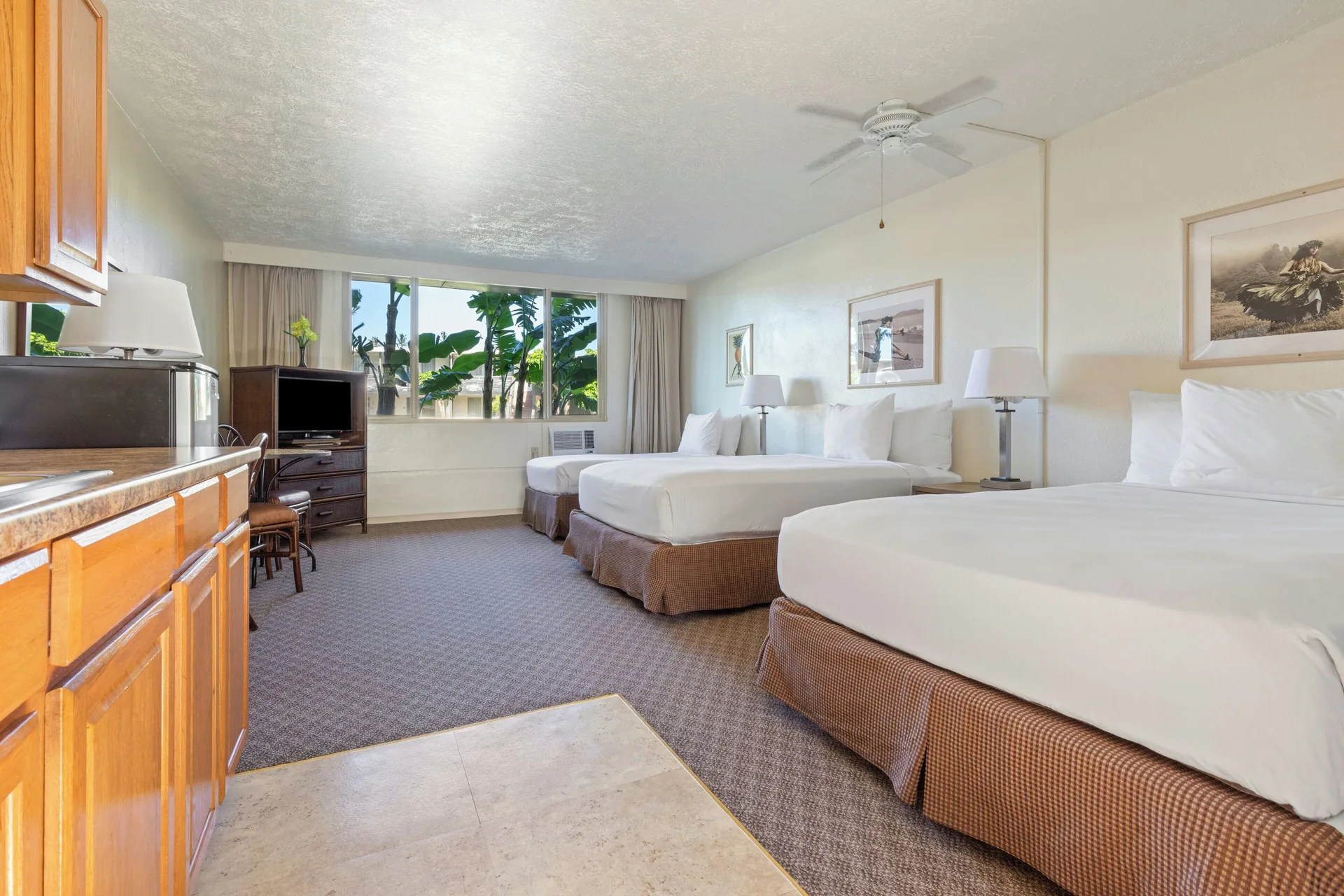 Poolside room with three beds, kitchenette, TV, and window greenery at Maui Seaside Hotel.