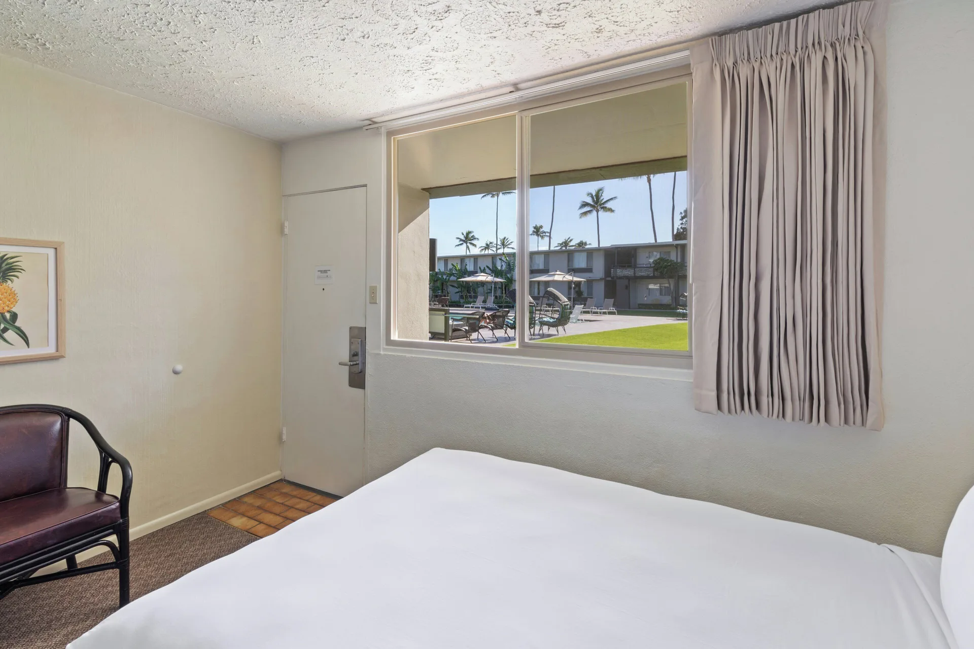 Poolside room with a bed, chair, and courtyard view at Maui Seaside Hotel.