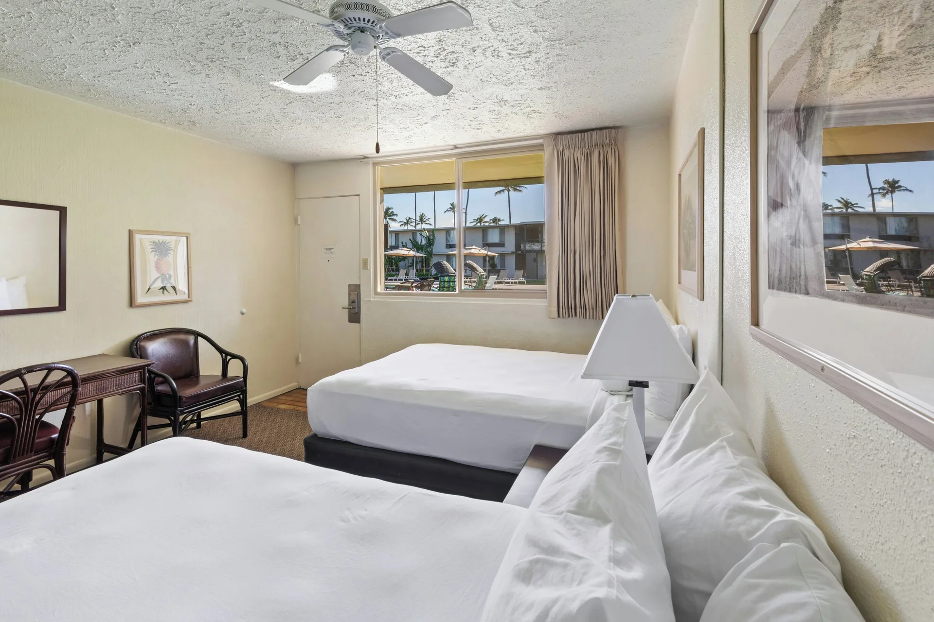 Poolside room with two beds, desk, chair, and courtyard window at Maui Seaside Hotel.