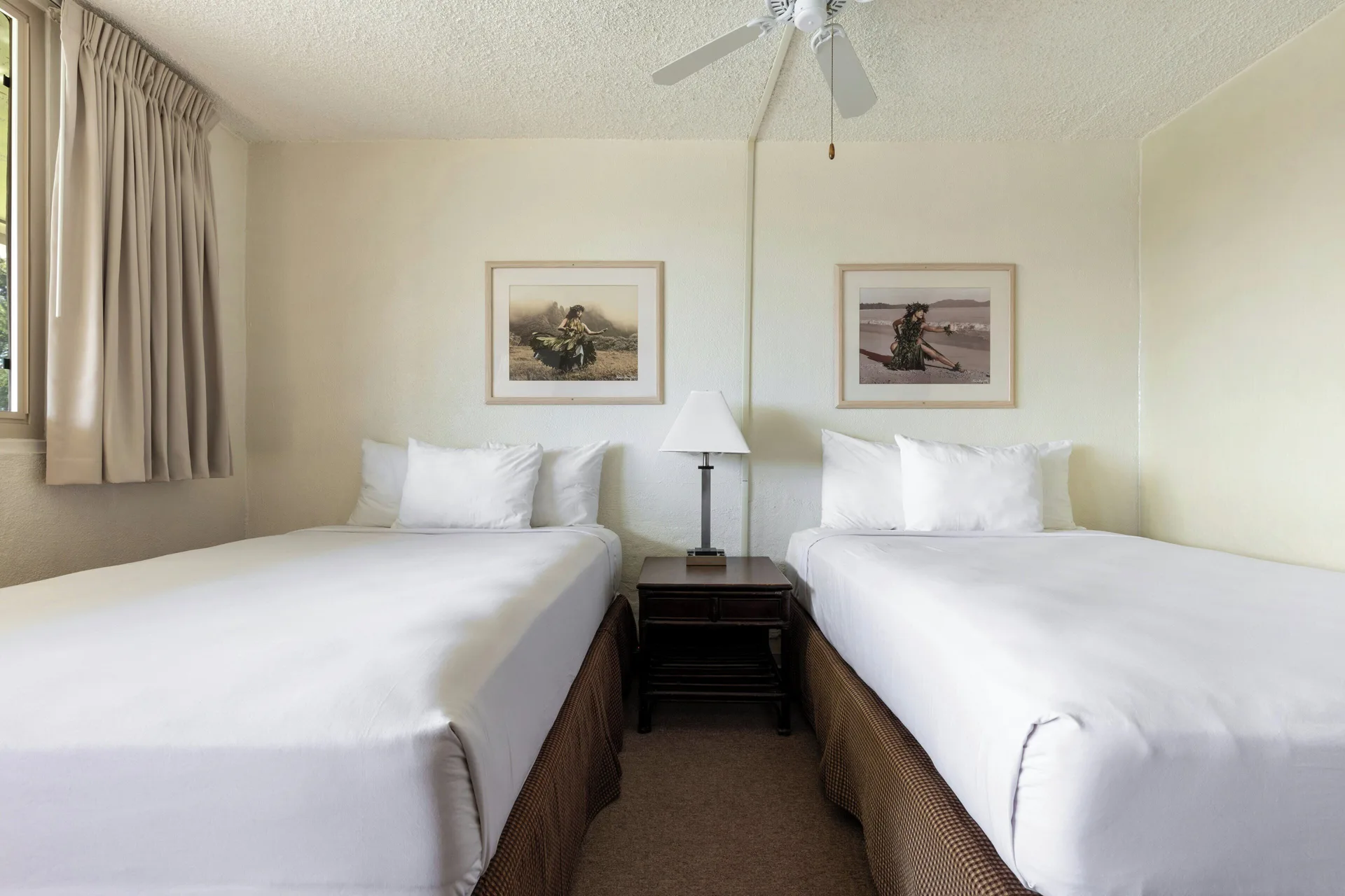 Poolside room with two beds, framed art, and a ceiling fan at Maui Seaside Hotel.