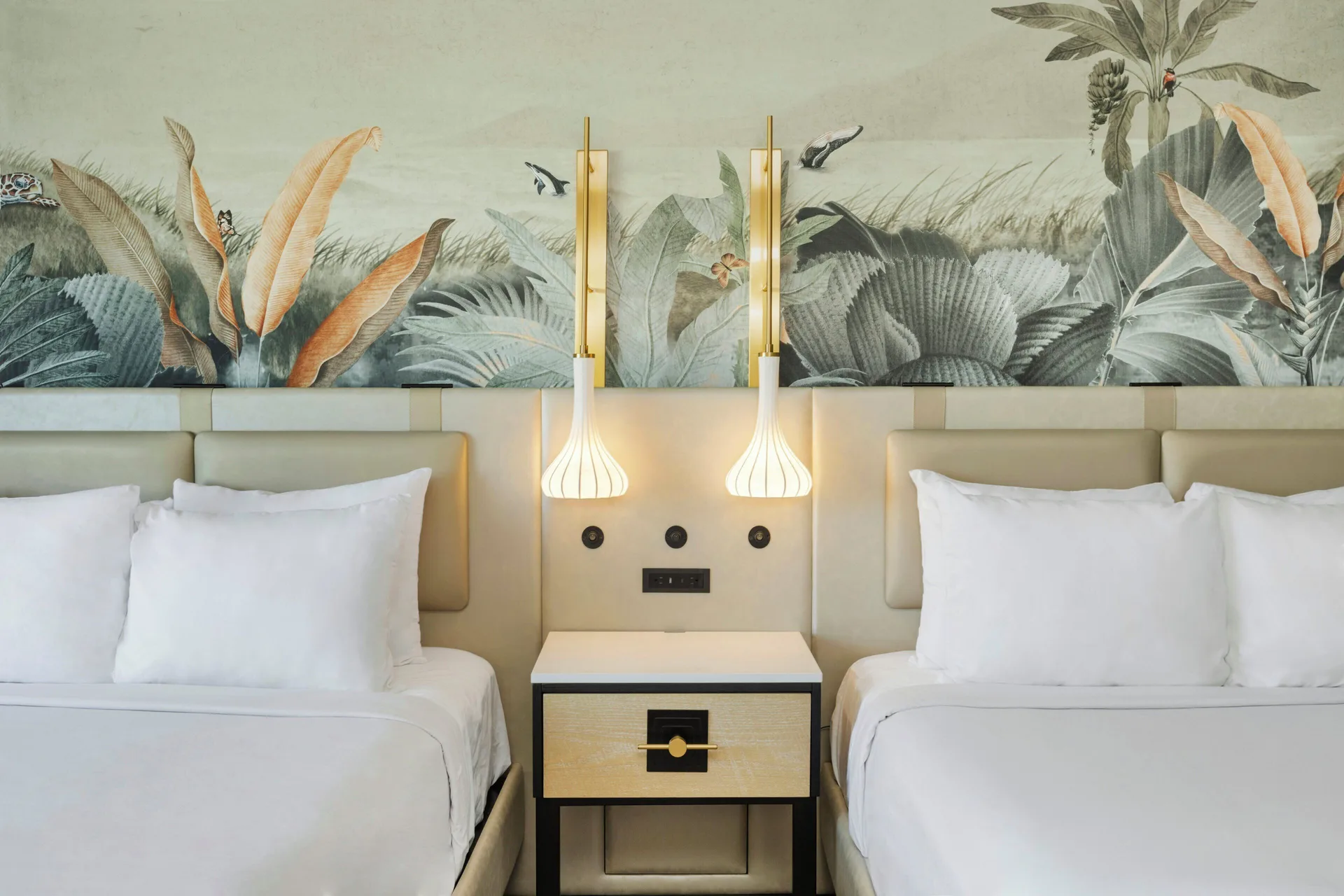 Two guest room beds with pendant lights and tropical mural at Maui Seaside Hotel.