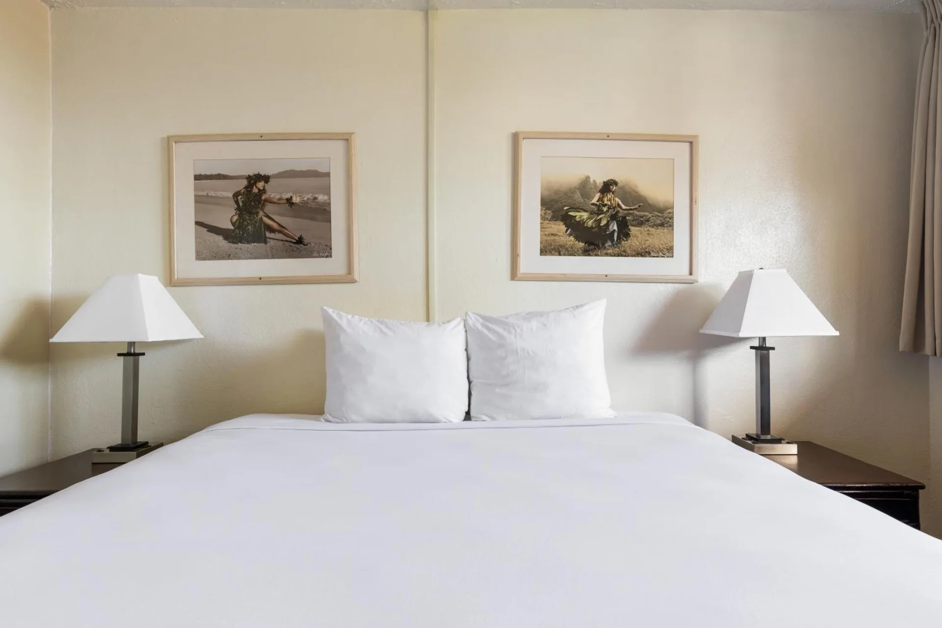 Standard One bed with white linens, framed artwork and two bedside lamps at Maui Seaside Hotel.