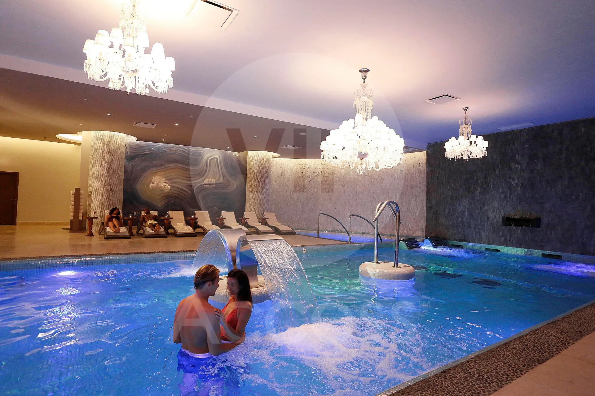 Indoor spa pool with chandeliers, loungers, and guests in the water at Moon Palace Jamaica.