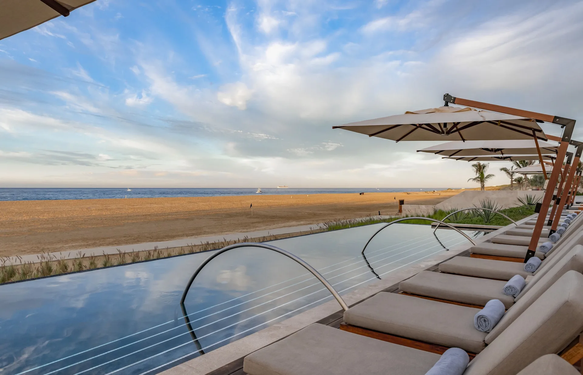 Beachfront infinity pool with loungers and umbrellas at Nobu Hotel Los Cabos.