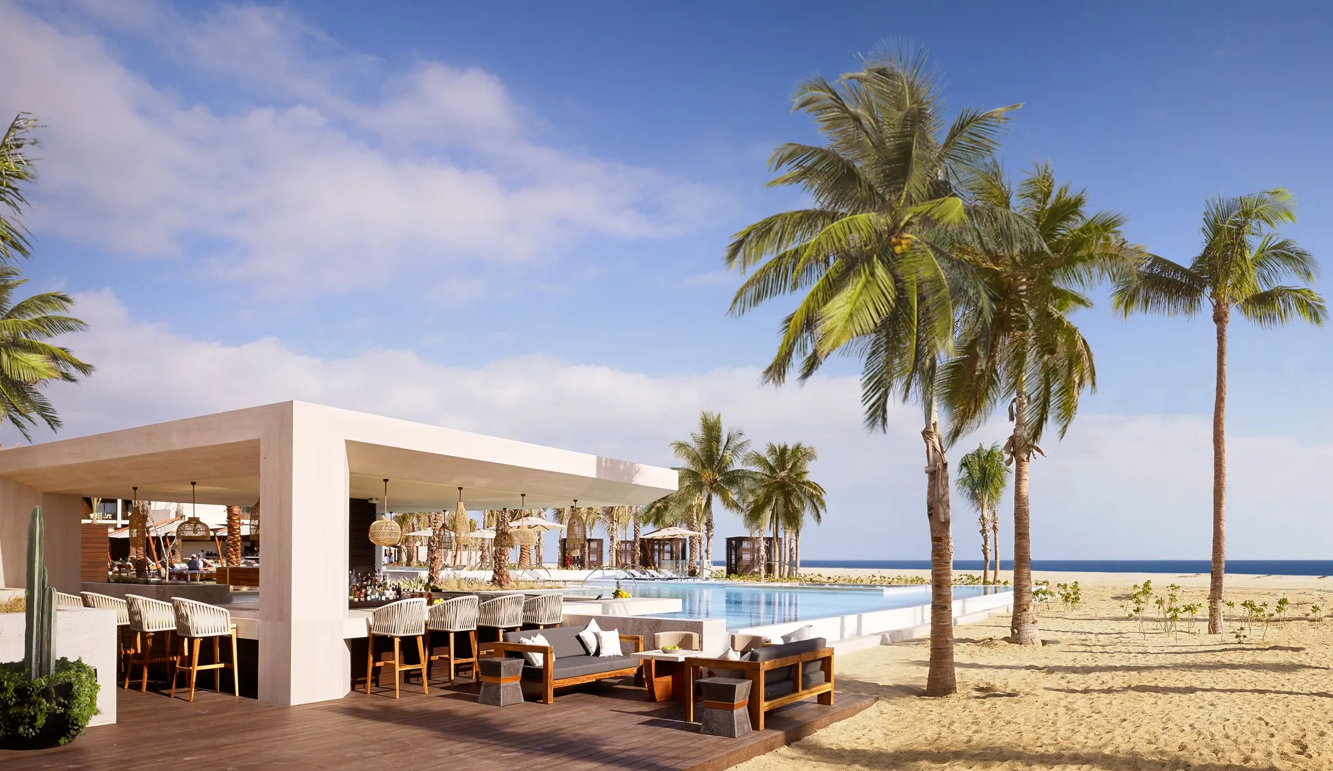 Open-air beachfront bar, pool, palms, and seating at Nobu Hotel Los Cabos.
