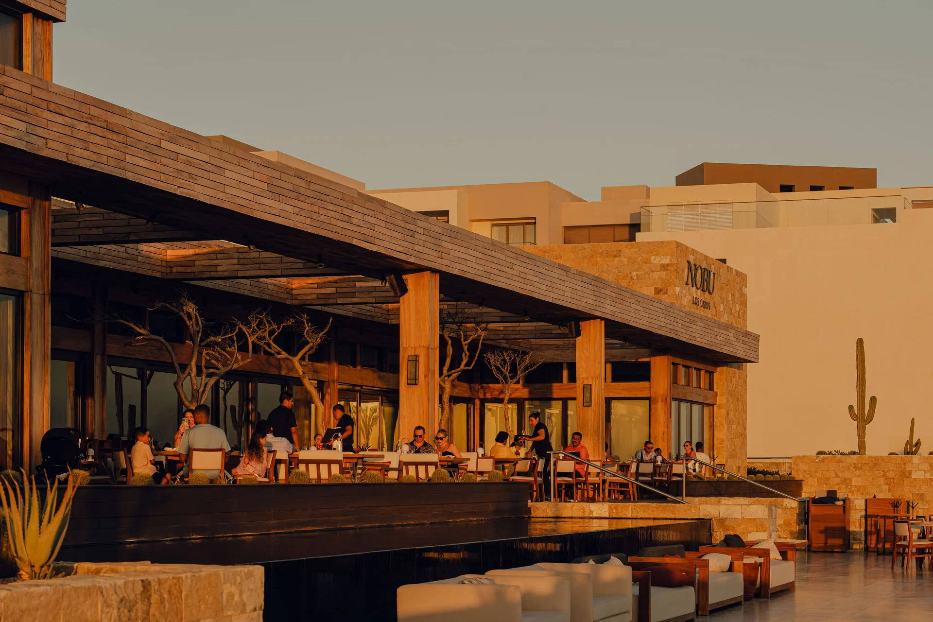 Nobu Hotel Los Cabos restaurant patio with diners in golden light at Nobu Hotel Los Cabos.