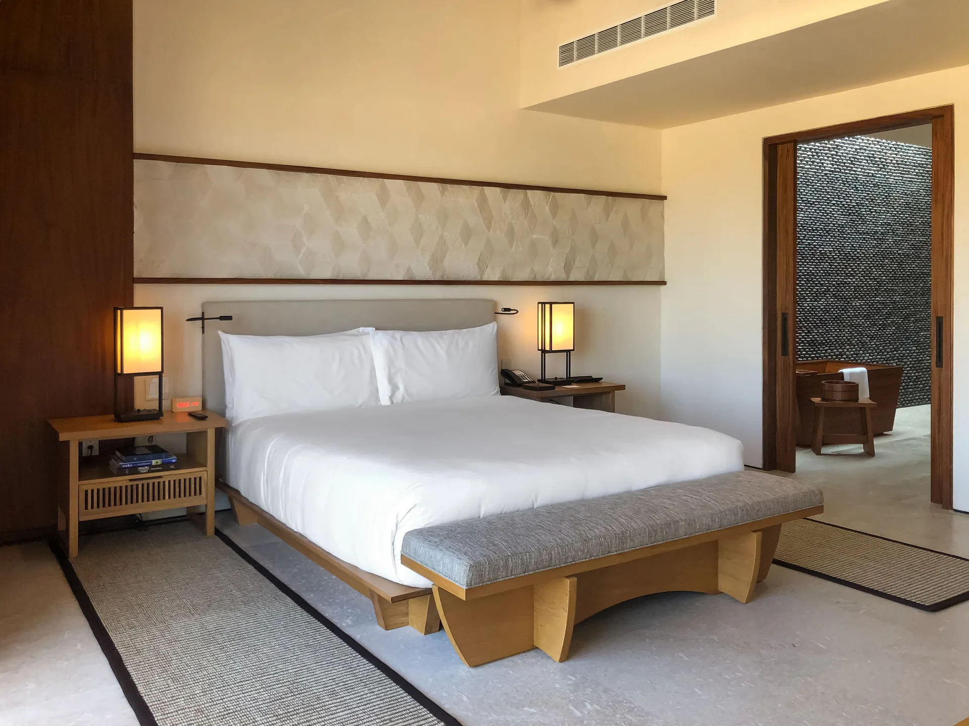 Deluxe Room king bed with bench and bathroom doorway at Nobu Hotel Los Cabos.