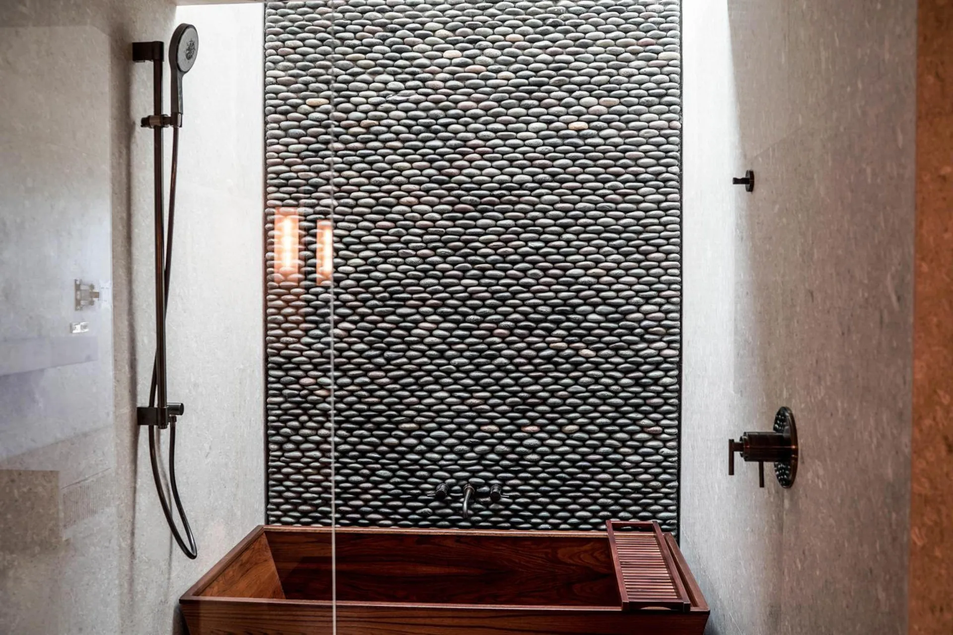 Deluxe bathroom wet room with wooden soaking tub and pebble wall at Nobu Hotel Los Cabos.