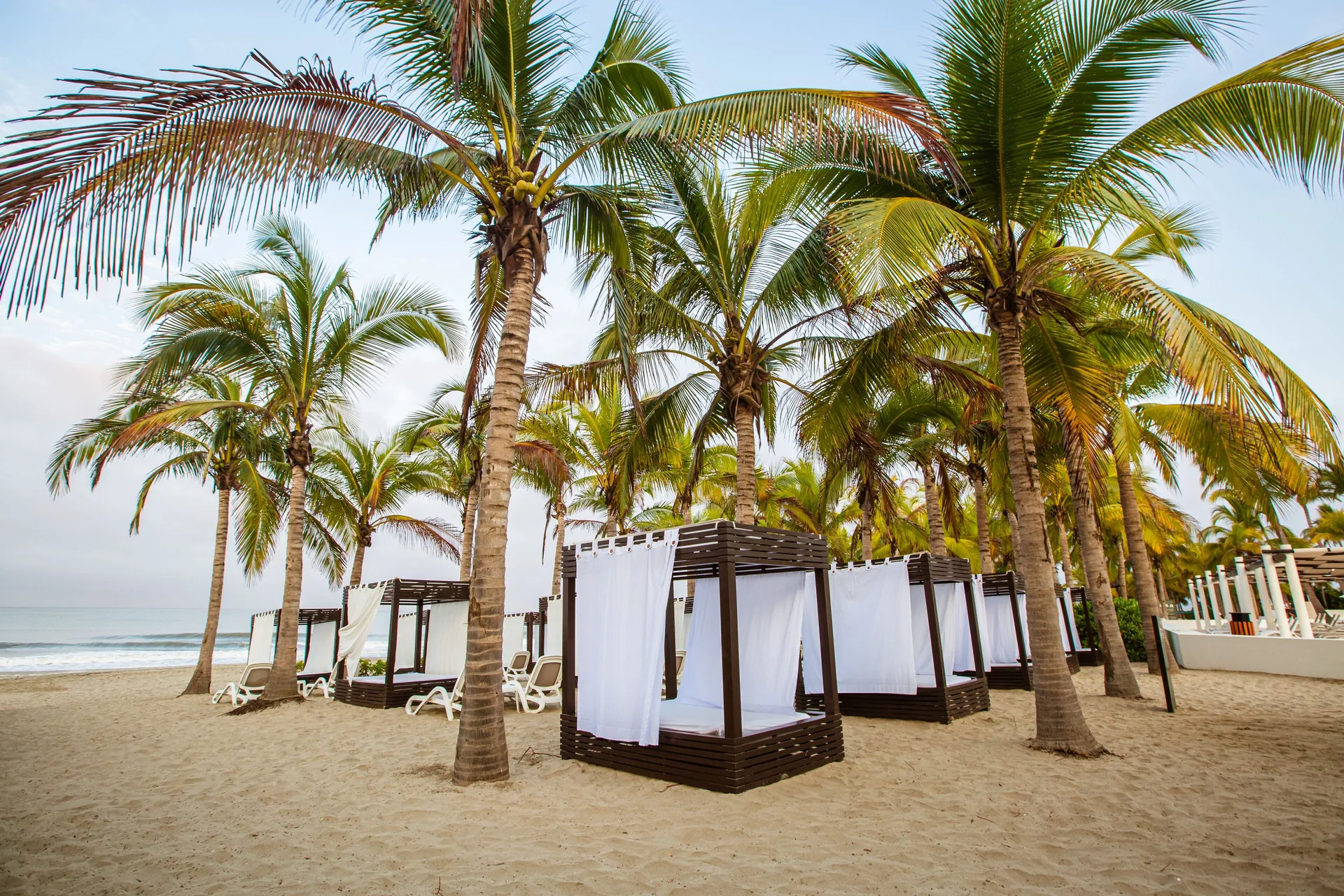 Beach cabanas sit among palm trees on the sand at Occidental Nuevo Vallarta.