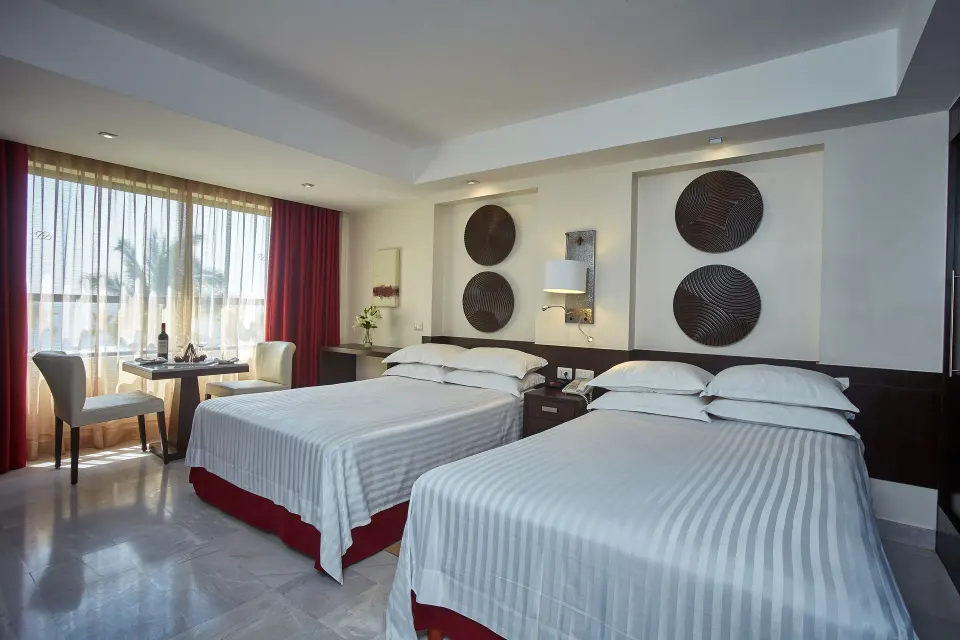 Deluxe Ocean View room with two beds, dining table, and window at Occidental Nuevo Vallarta.