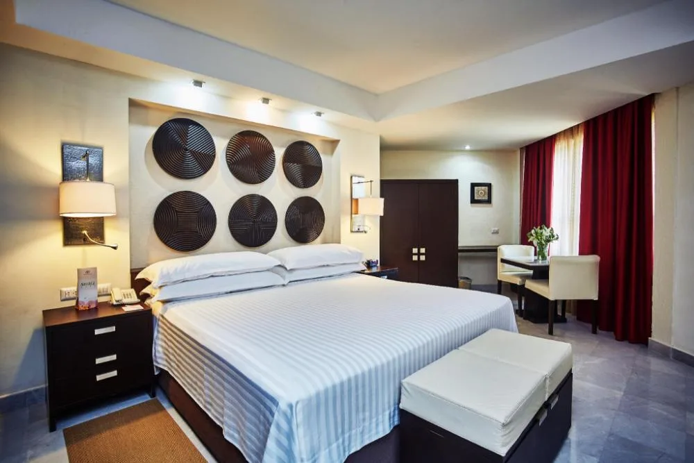 Deluxe king bed guest room with red curtains and seating at Occidental Nuevo Vallarta.