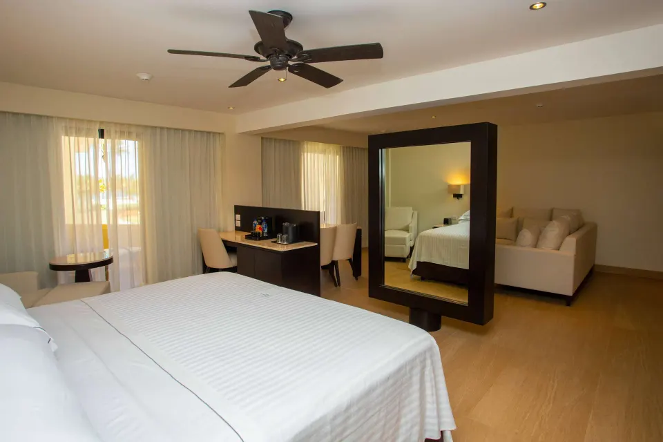 Junior Suite balcony room with king bed, desk, mirror, and sofa at Occidental Nuevo Vallarta.