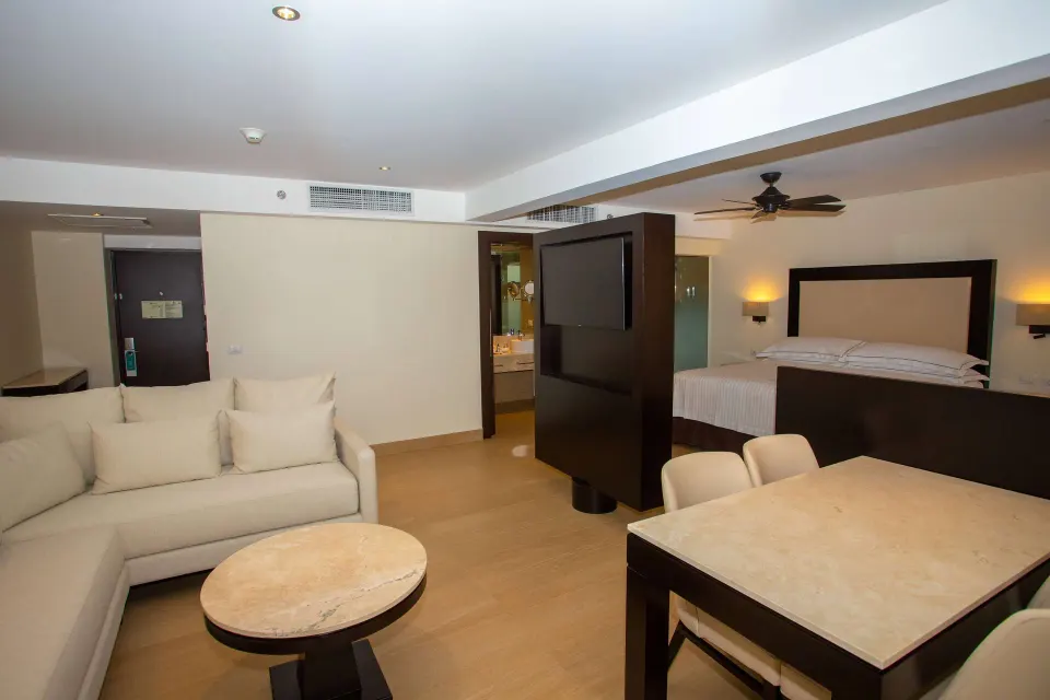 Junior Suite balcony room with king bed, sofa, dining table, and TV divider at Occidental Nuevo Vallarta.