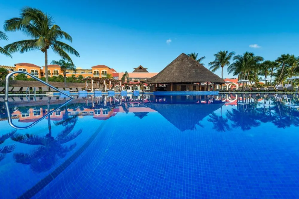 Large pool with palapa bar, palm trees, and resort buildings at Ocean Coral and Turquesa.