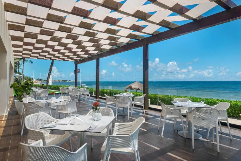Oceanfront dining terrace with white tables and chairs at Ocean Coral and Turquesa.