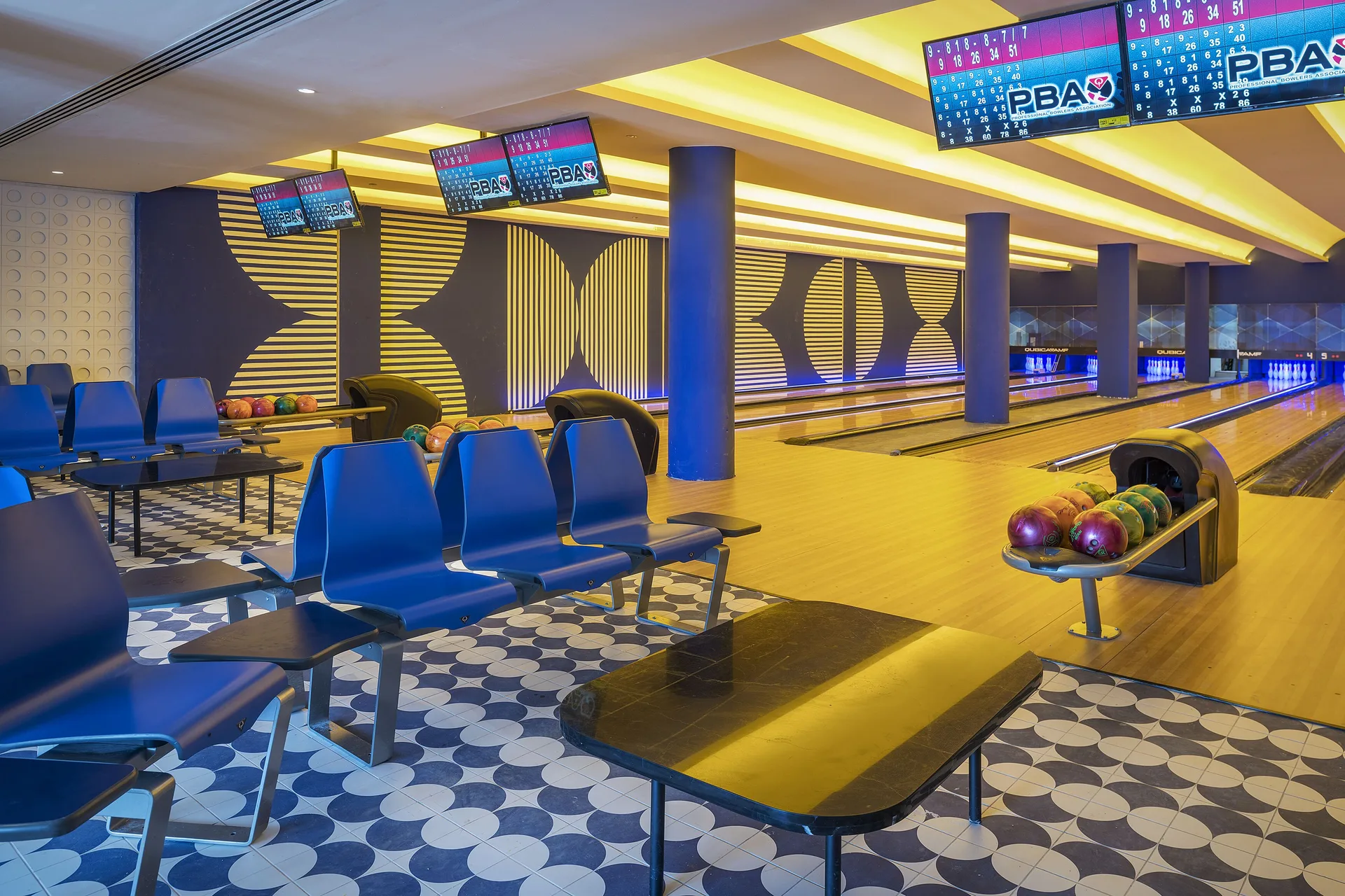 Bowling alley lanes with ball racks and blue seating at Ocean Coral Spring.