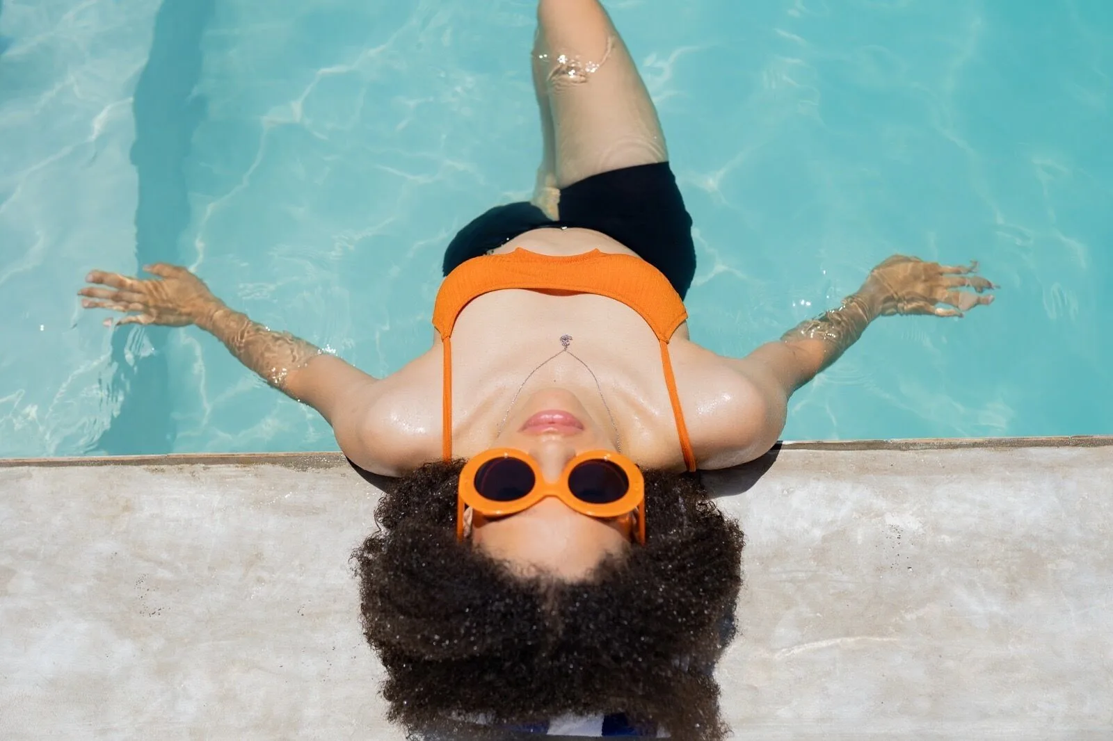 Guest in orange sunglasses floating at the pool edge at Orient Beach Hotel.