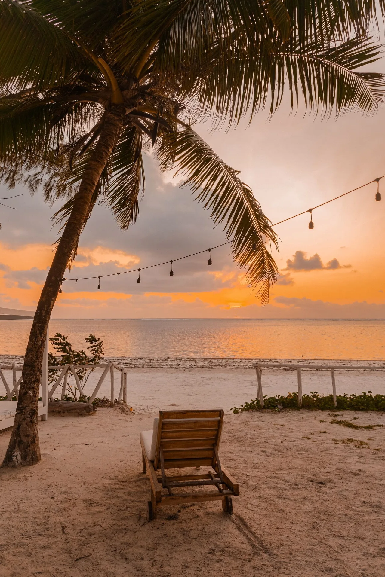 A lounge chair faces the ocean at sunset beneath a palm at Orient Beach Hotel.