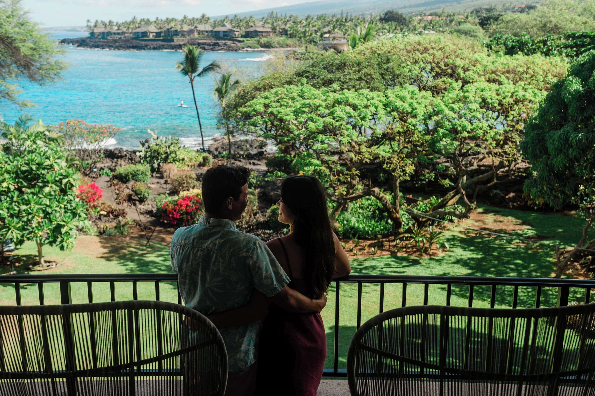 Couple on a balcony overlooking gardens and the ocean at Outrigger Kona Resort and Spa.