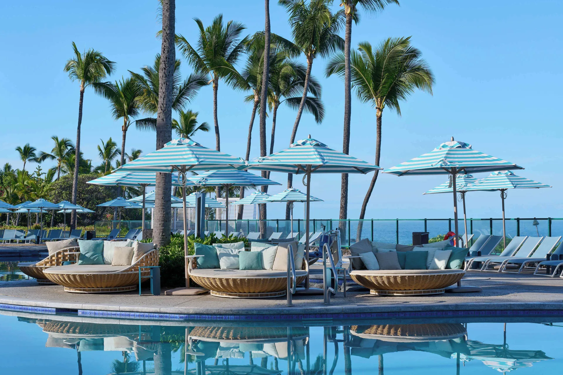 Poolside daybeds and striped umbrellas by the water at Outrigger Kona Resort and Spa.