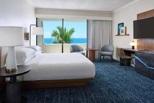 Suite king bed beside a large ocean-facing window at Outrigger Kona Resort and Spa.