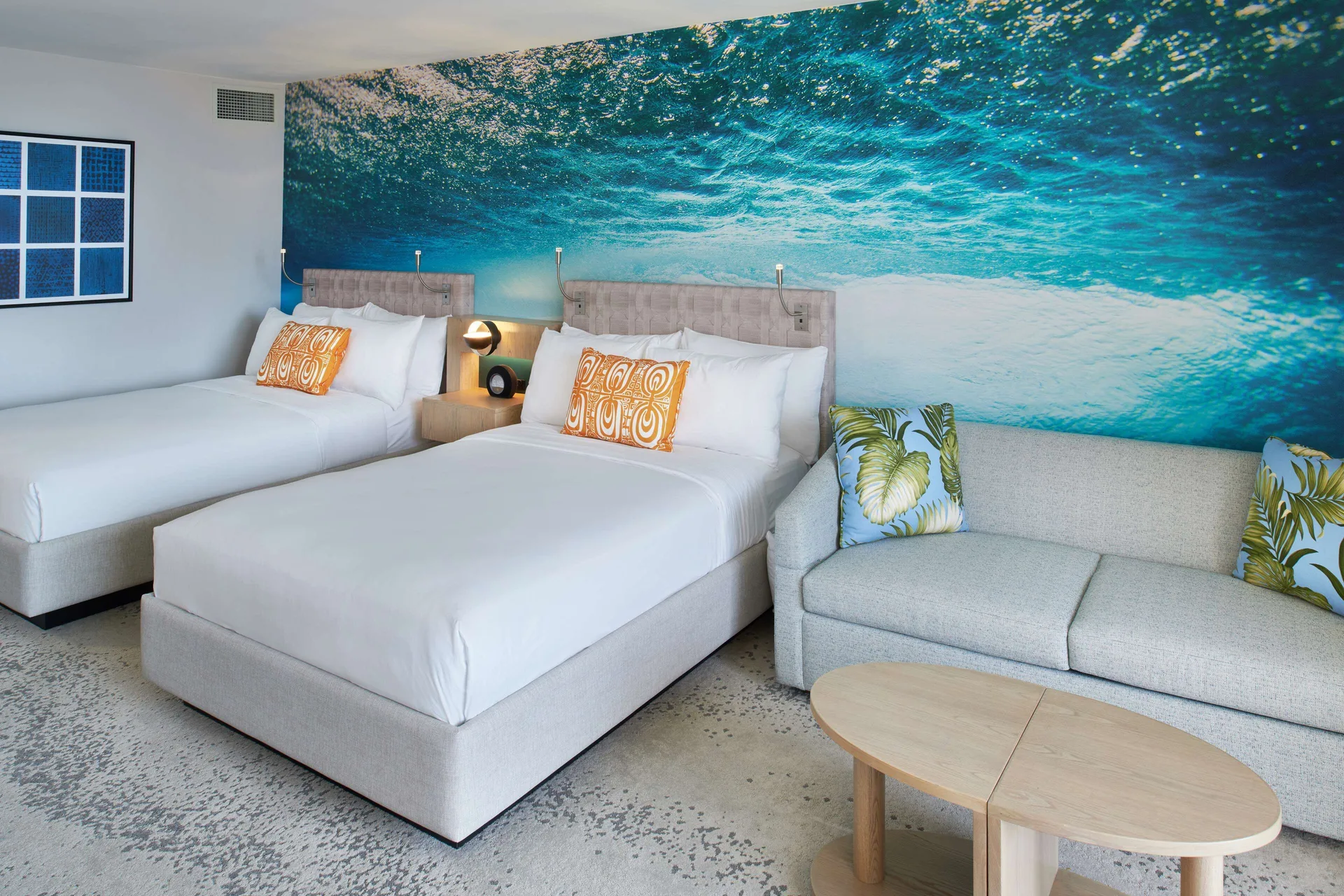 Junior Suite with two beds, ocean mural, sofa and round tables at OUTRIGGER Waikiki Beachcomber Hotel.
