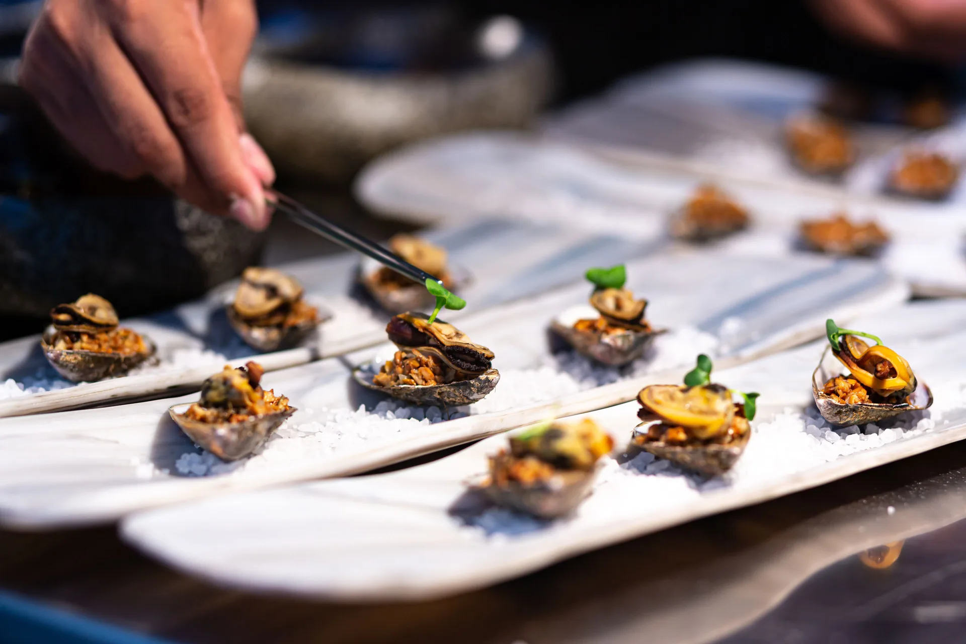 Small shellfish bites being garnished on plates at Paradisus La Perla Riviera Maya.