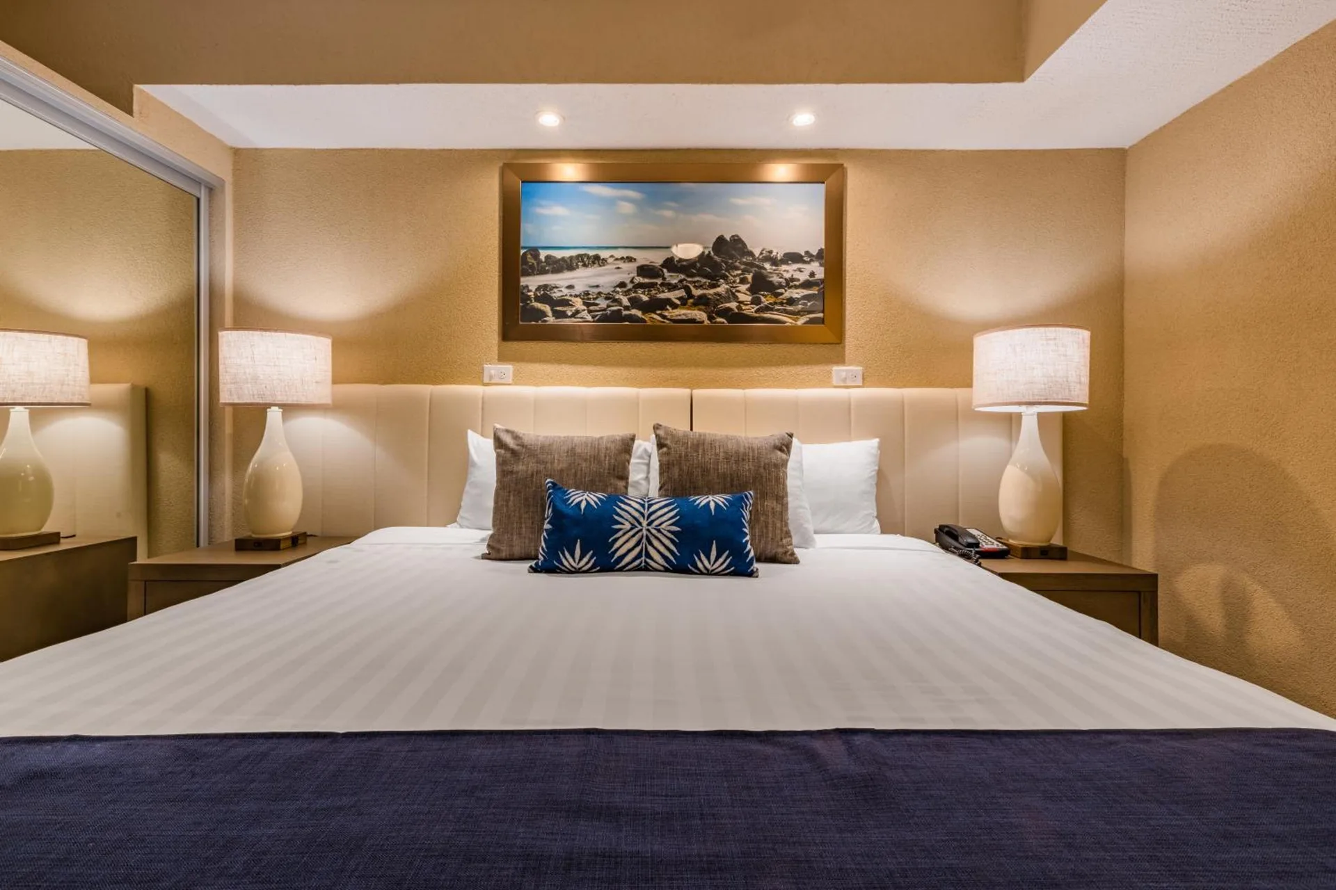 Guest bedroom with king bed, lamps, and beach artwork at Playa Linda Beach Resort.