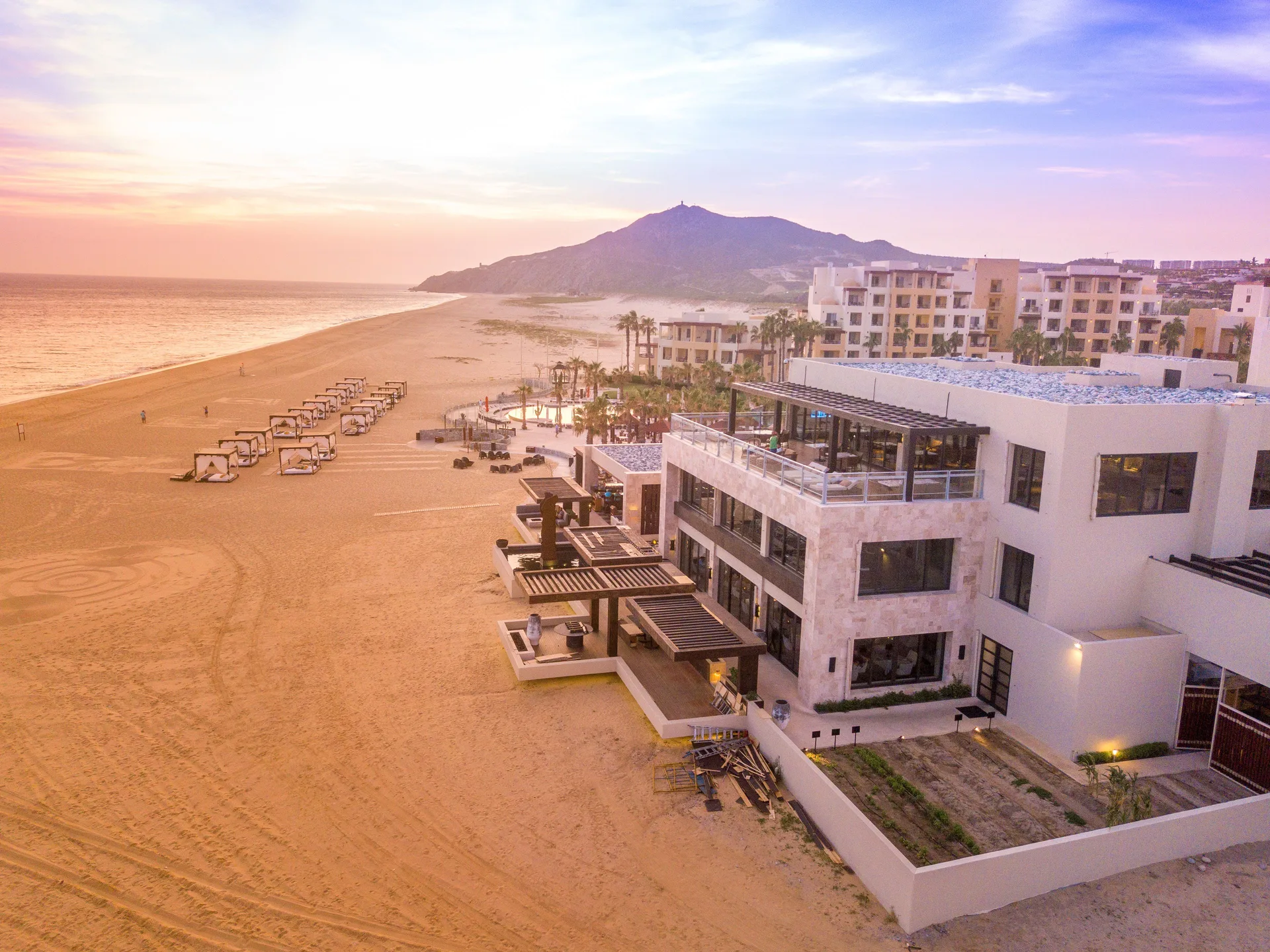 Beachside resort buildings at Pueblo Bonito Pacifica Golf & Spa Resort beside cabanas and sand at sunset.