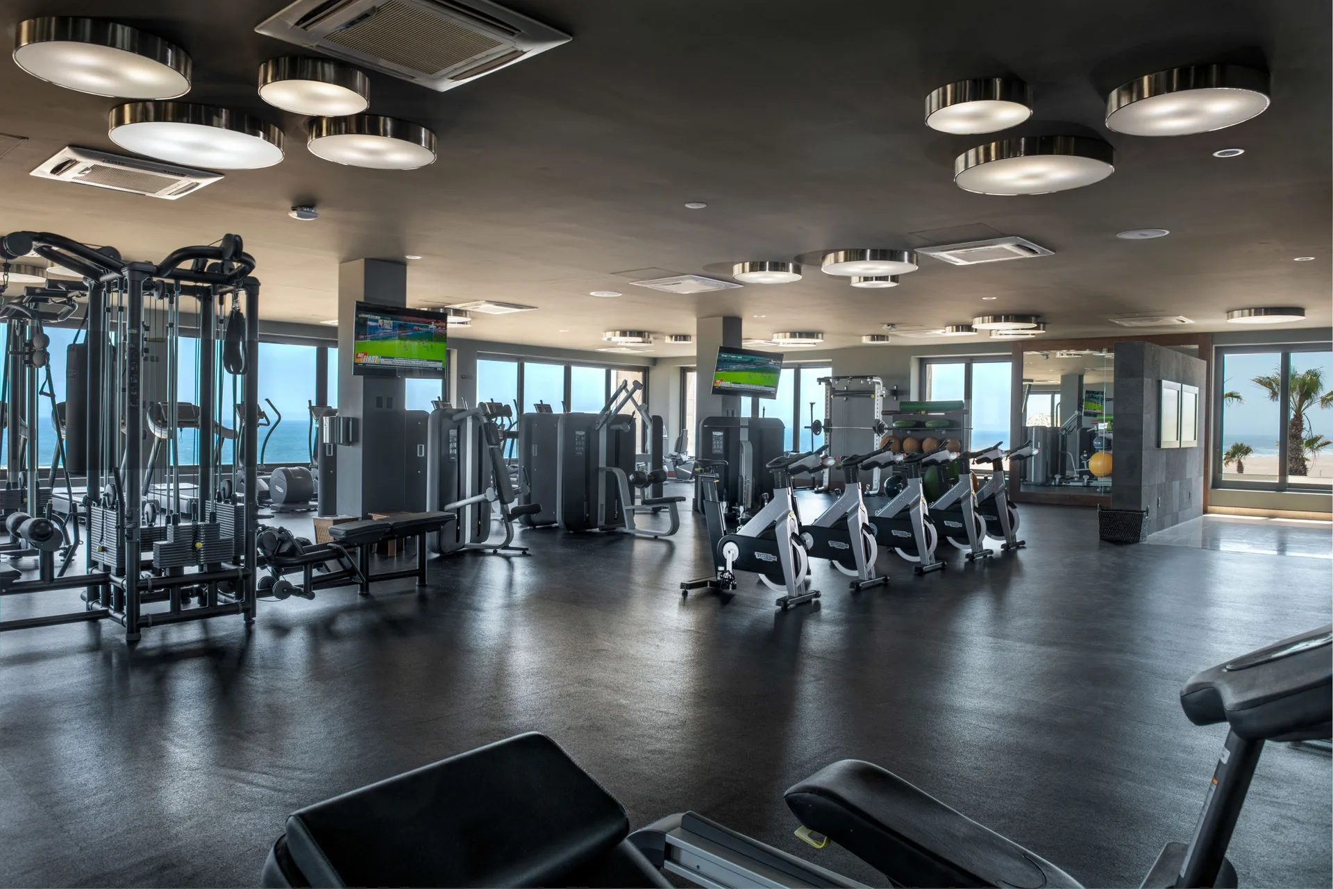 Fitness center with cardio machines, weight equipment, TVs, and ocean-facing windows at Pueblo Bonito Pacifica Golf & Spa Res
