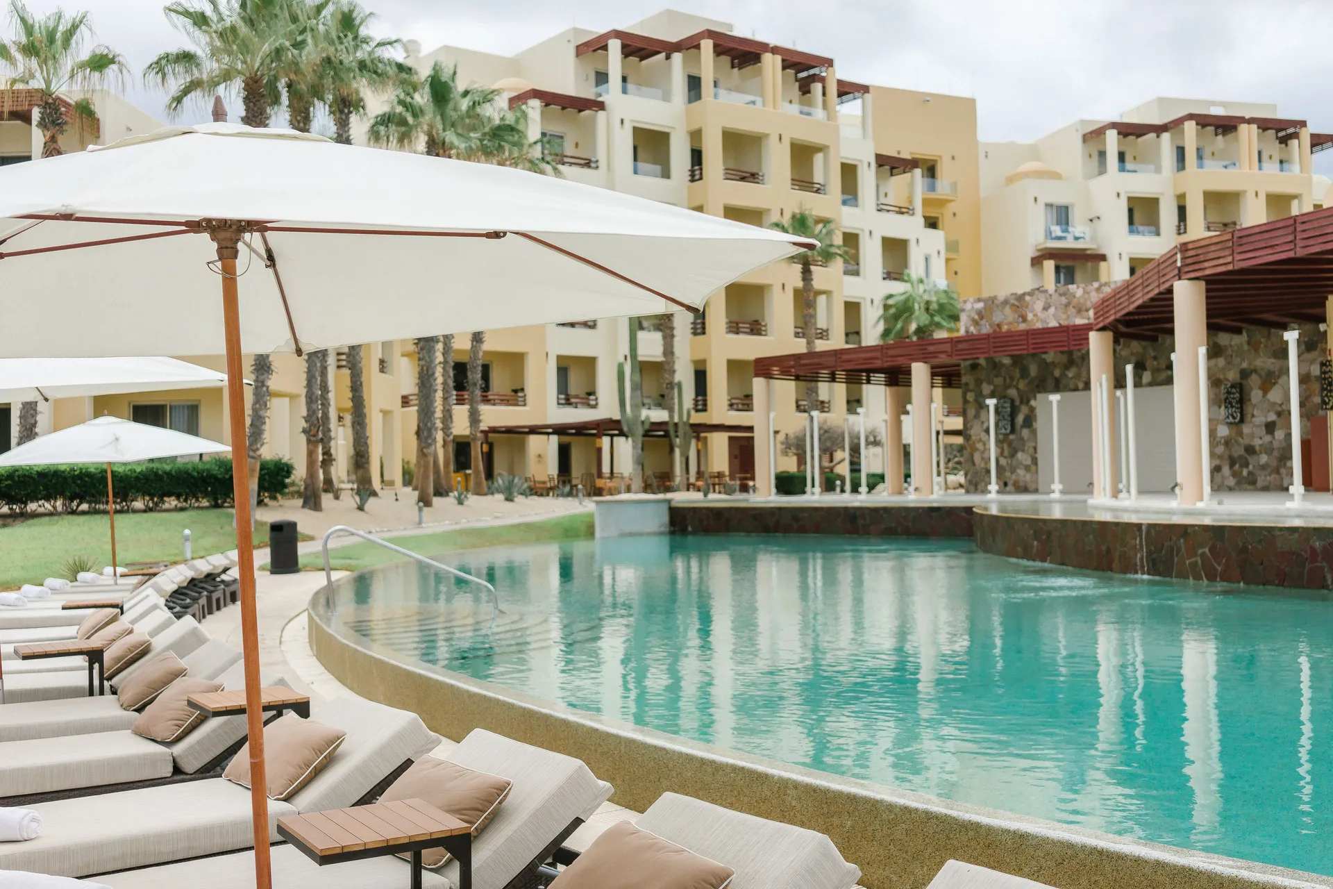 Pool with lounge chairs, umbrellas, and resort buildings at Pueblo Bonito Pacifica Golf & Spa Resort.