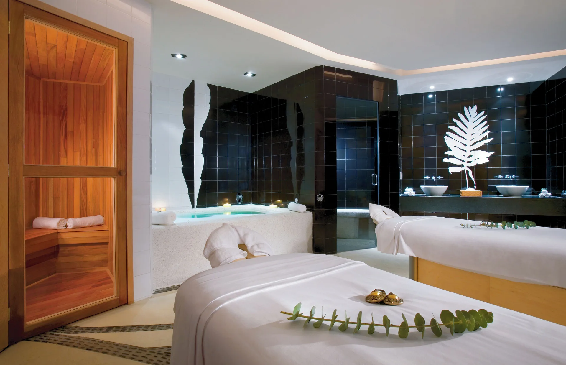 Spa suite with massage tables, sauna, soaking tub, and black tile accents at Pueblo Bonito Pacifica Golf & Spa Resort.