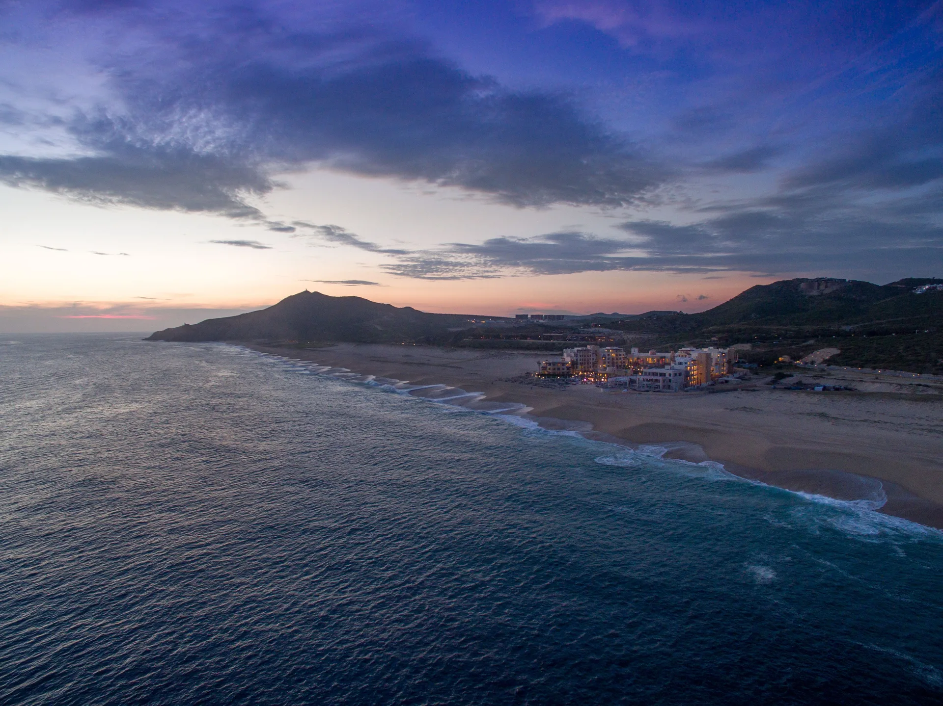 Twilight aerial coastline view with Pueblo Bonito Pacifica Golf & Spa Resort lit beside the beach.